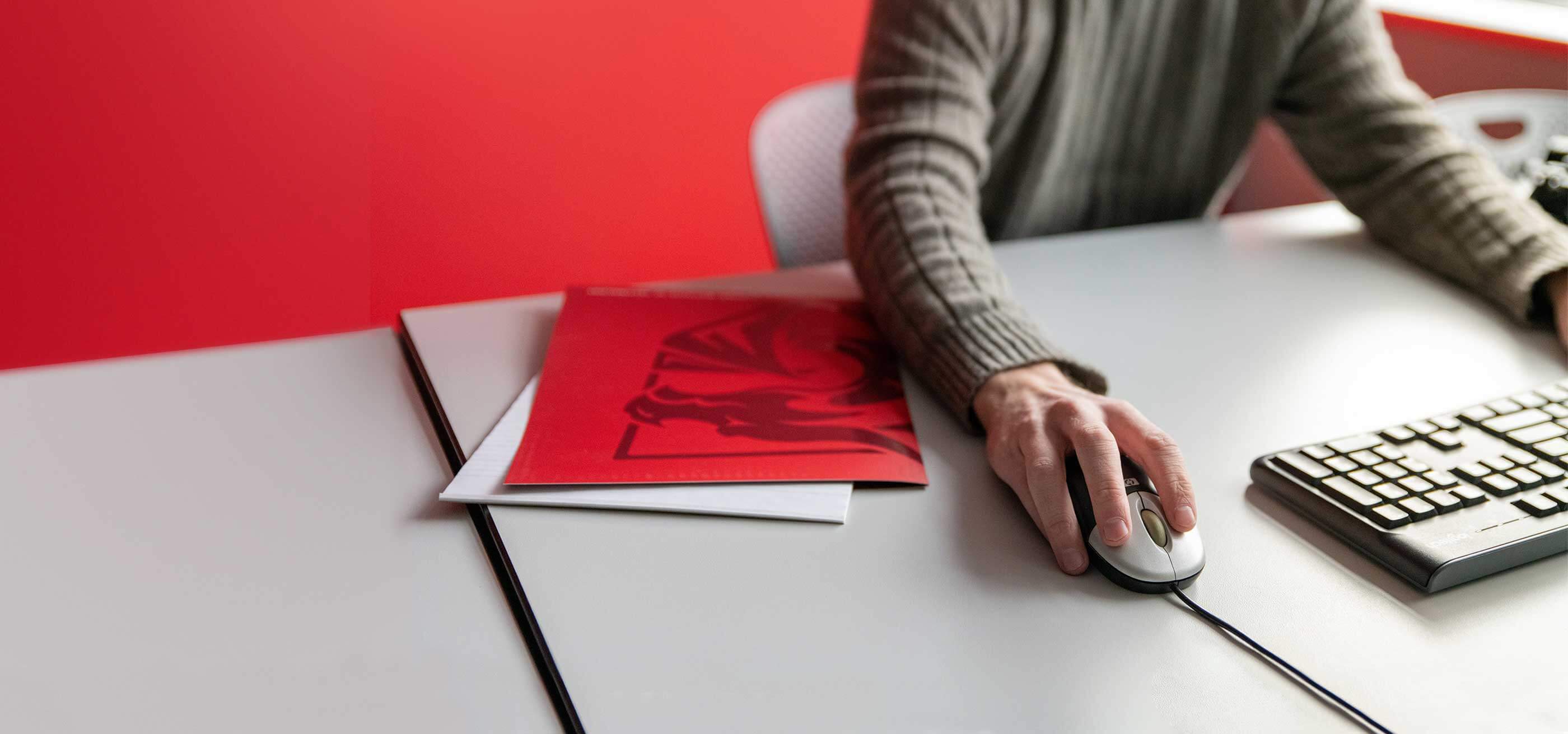 Angled view of a male faculty member using a mouse next to a DigiPen branded red folder.