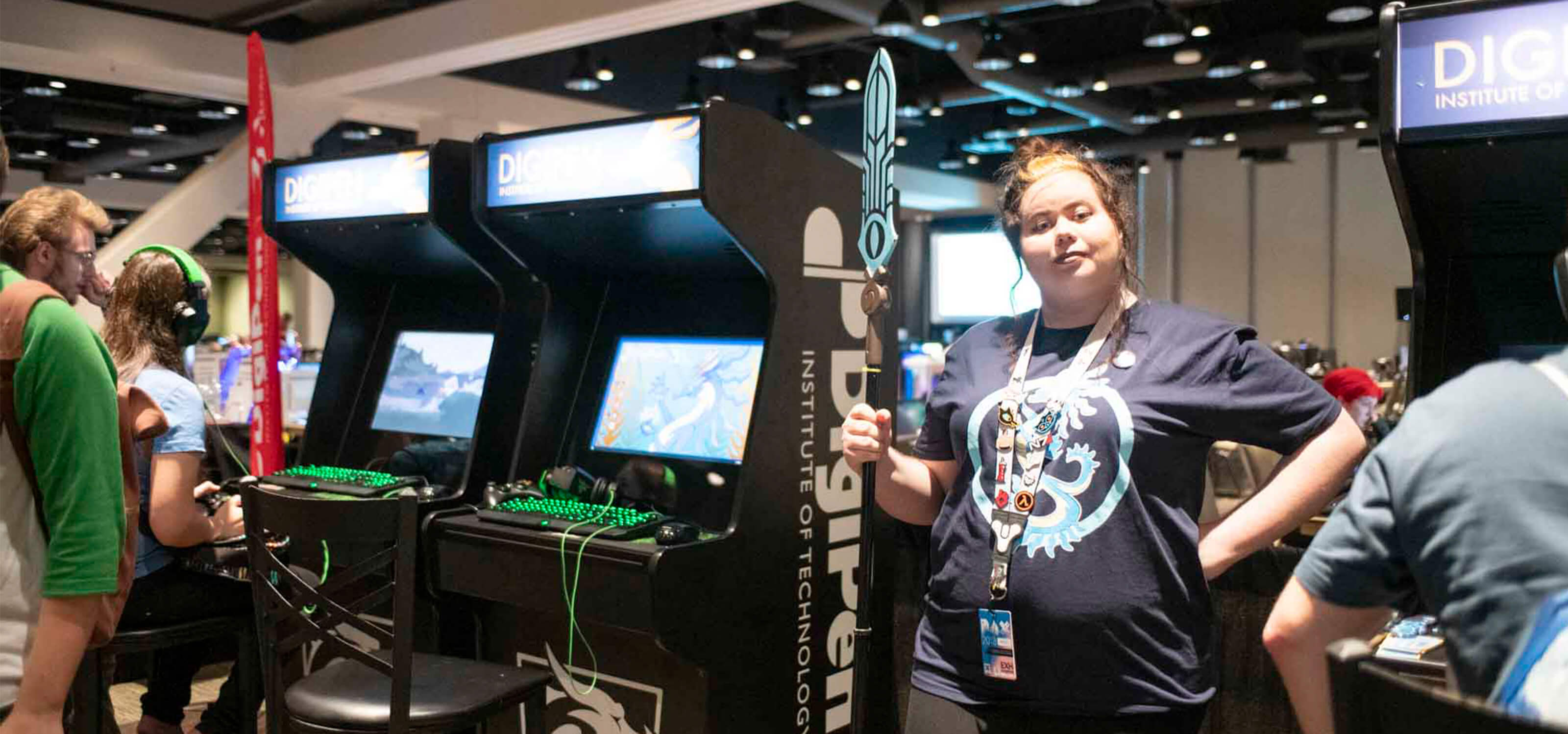 A DigiPen student staffs the PAX DigiPen arcade, cosplay spear in hand.