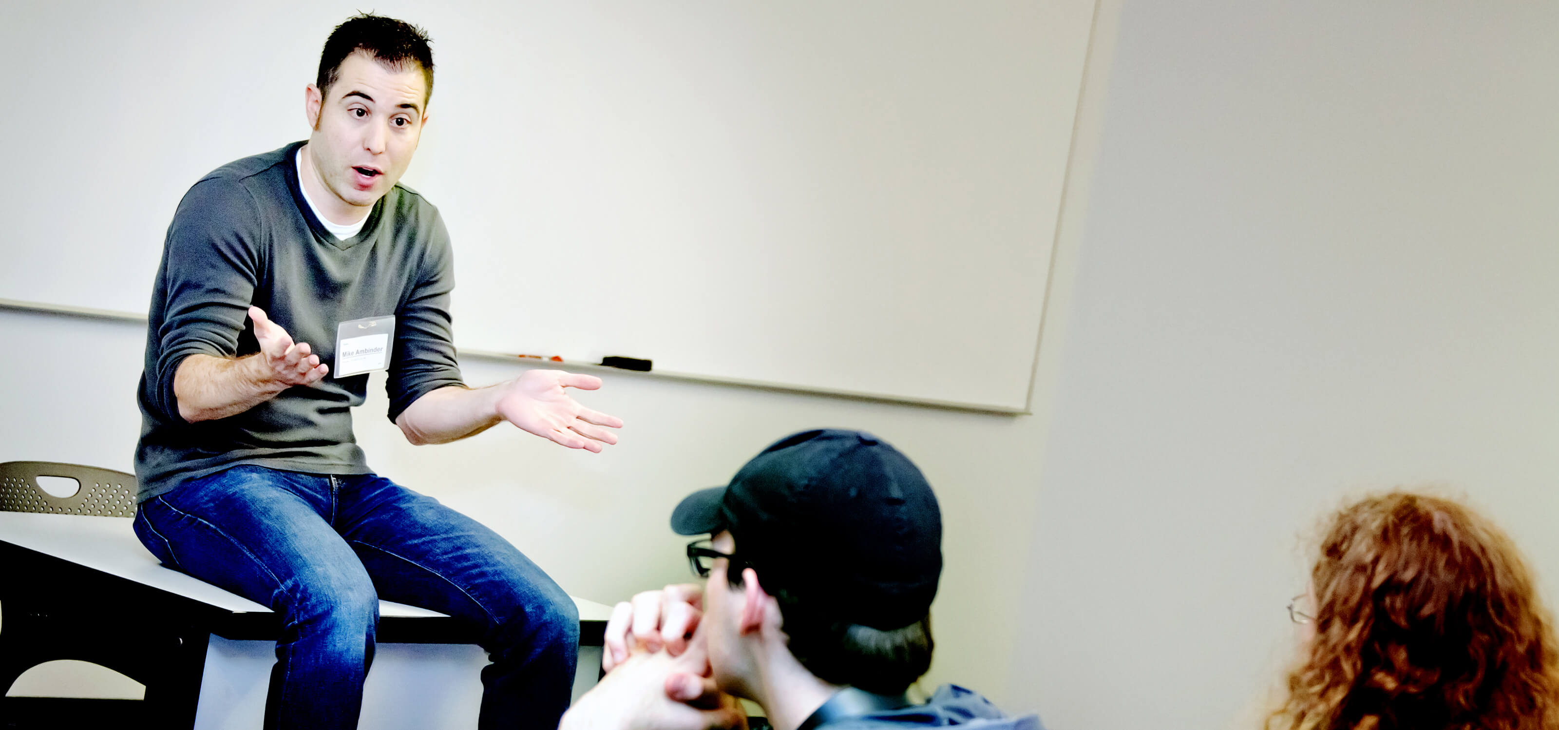 Mike Ambinder sitting on a table, talking to students in a DigiPen classroom