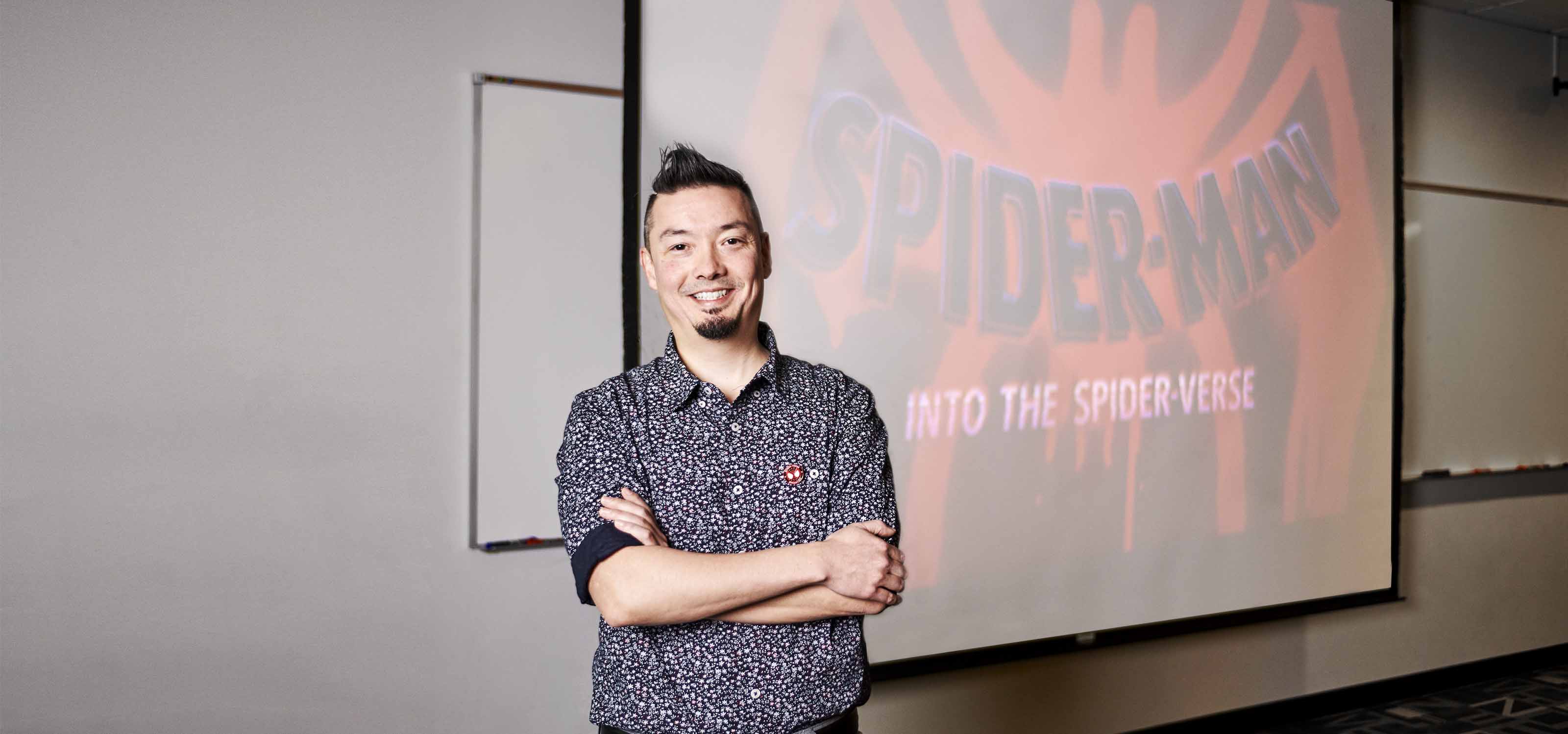 Nick Kondo smiles in front of a projection of Spider-Man: Into the Spider-Verse’s title card.