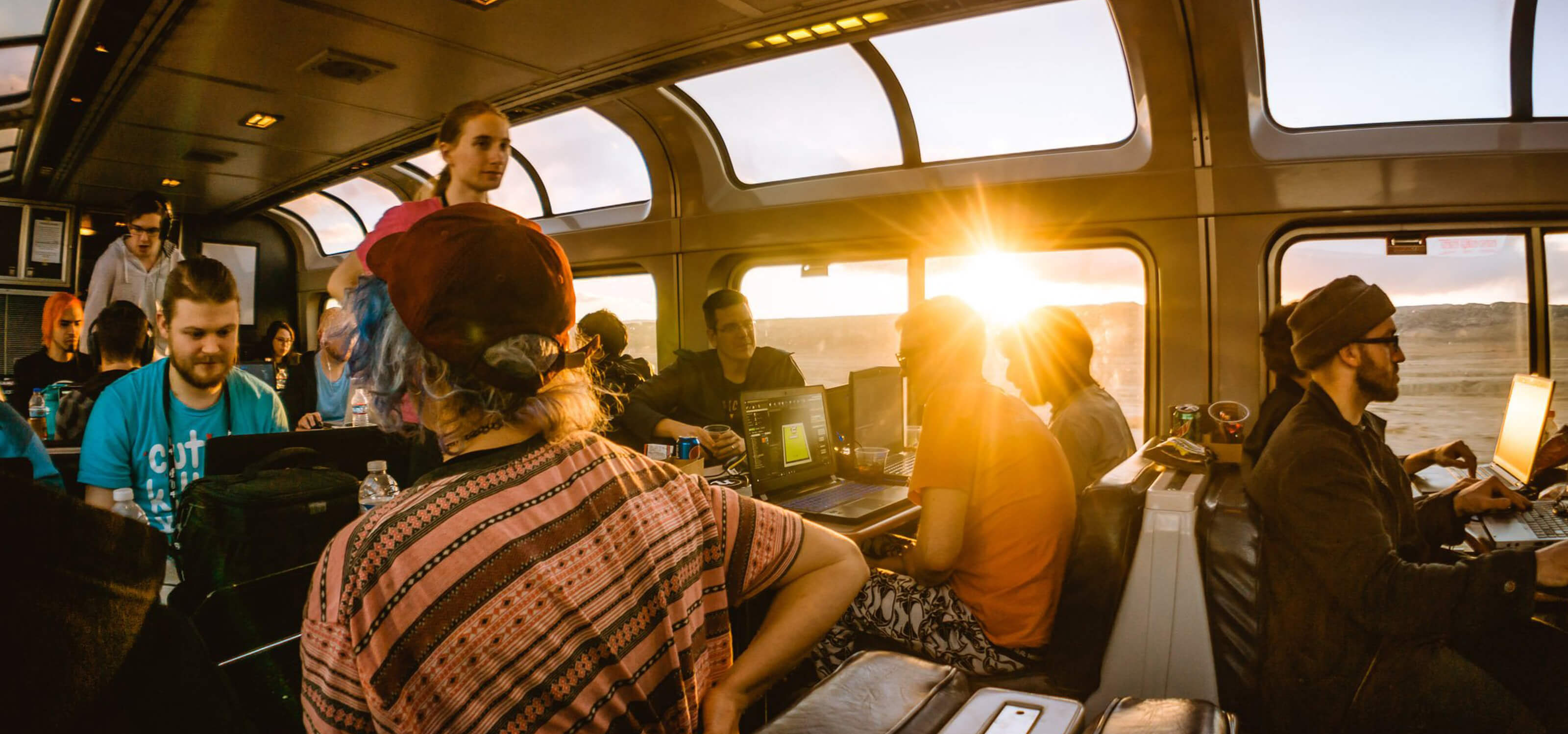 Afternoon sun beaming through the windows of the train's observation car where gamers collaborate on their laptops