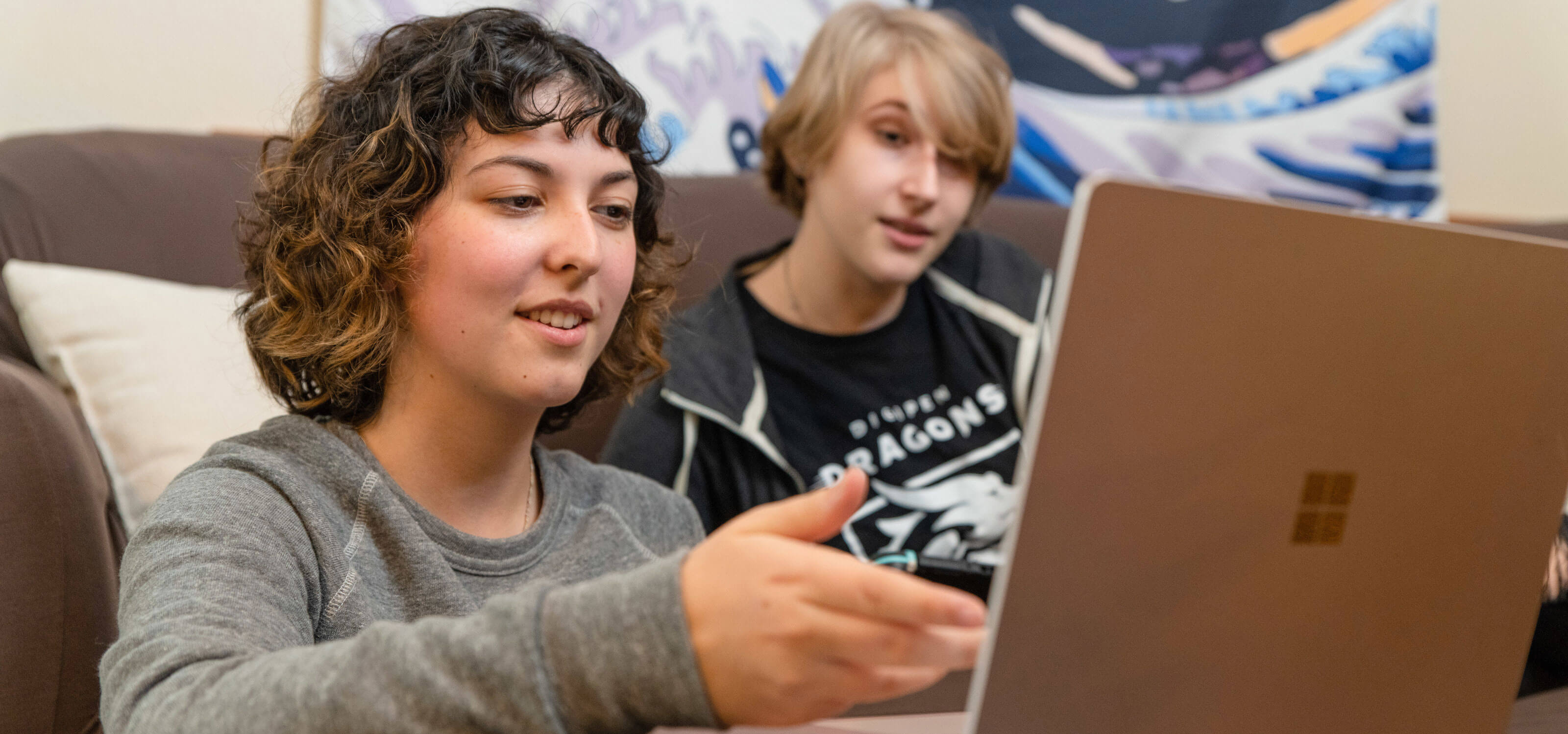 A female and male student sit and look at laptop while conversing 