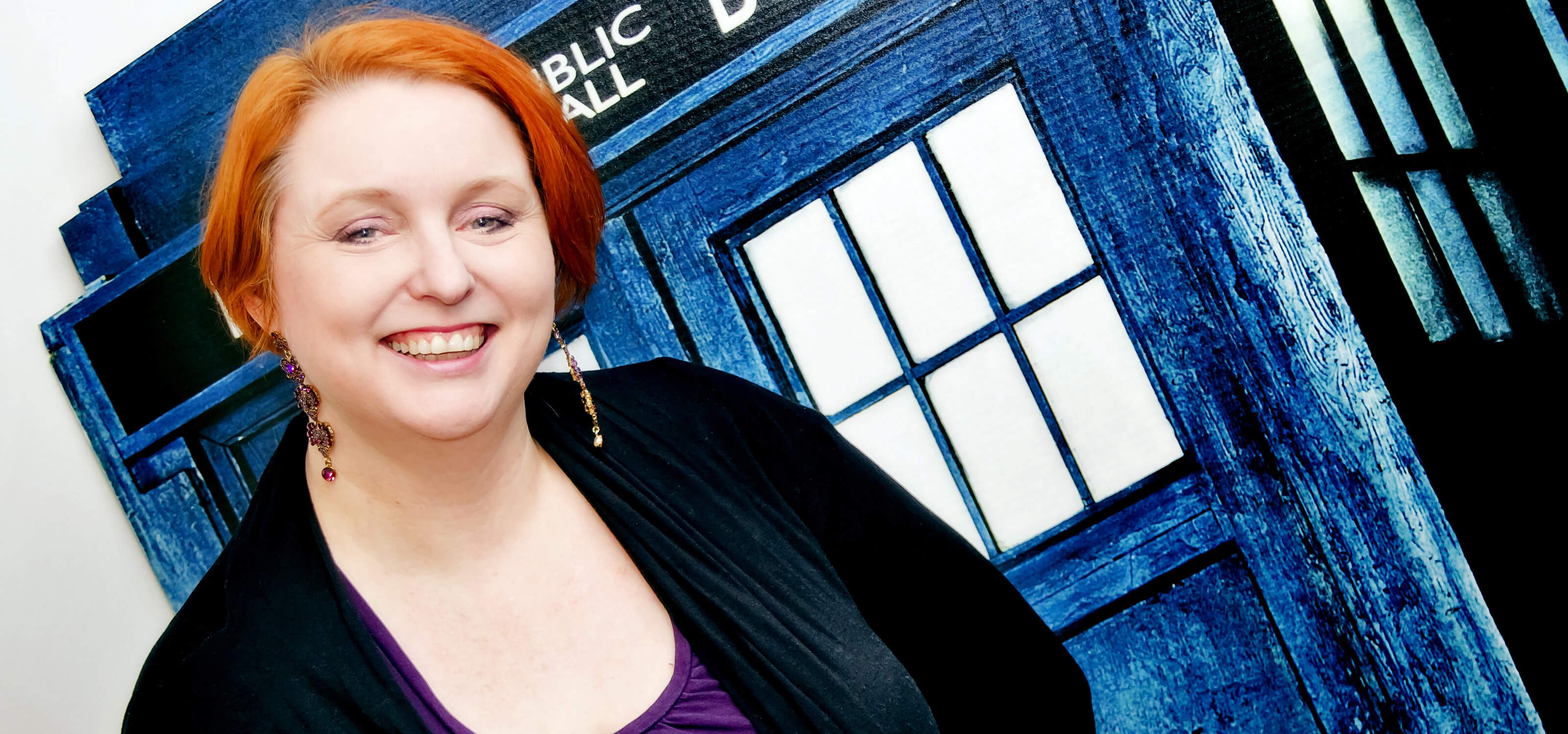 DigiPen lecturer Sonia Michaels smiling in front of the Dr. Who Tardis (a blue police box time machine) cutout in her office