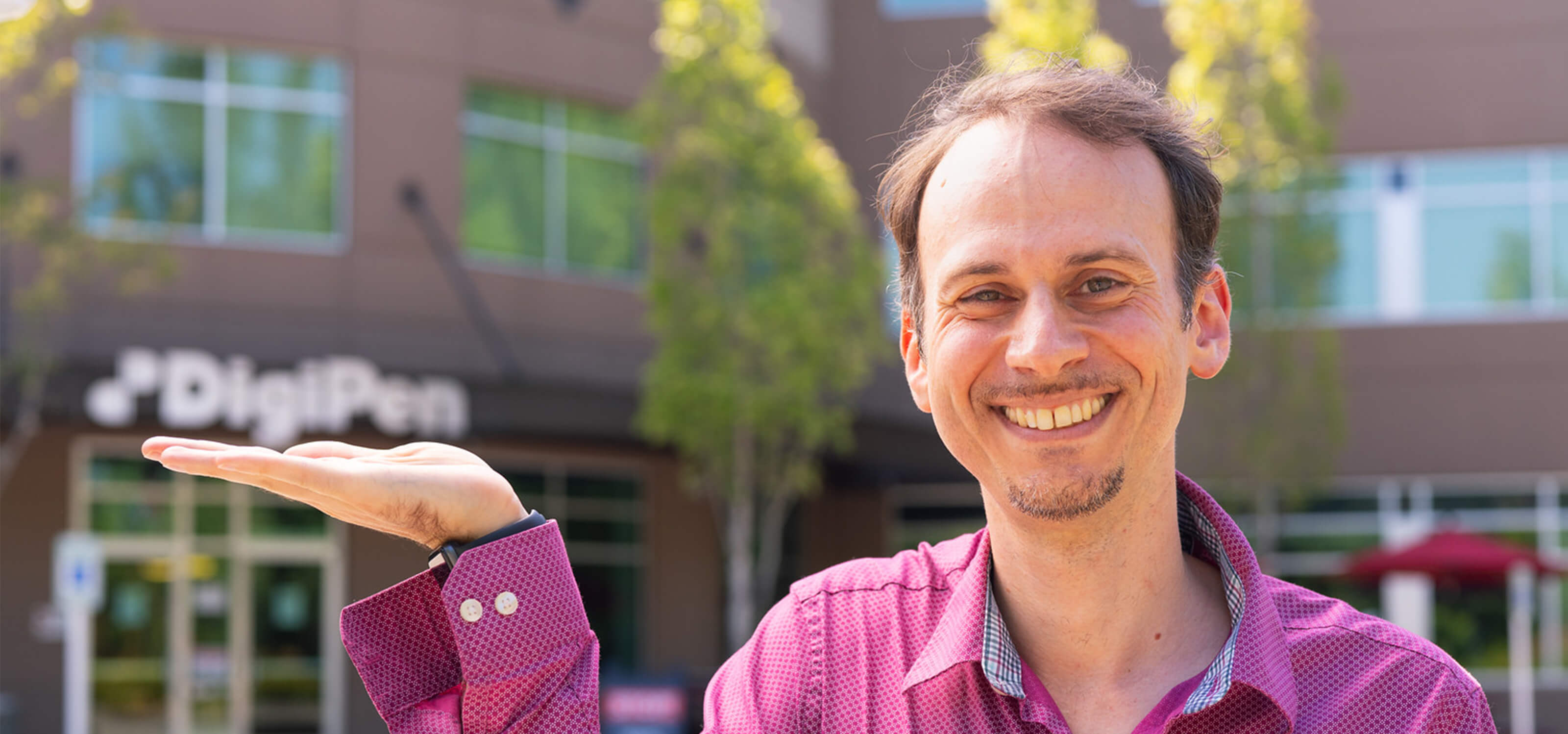 Alumnus Elliott Davis pretends to hold up the DigiPen sign on campus with his hand.