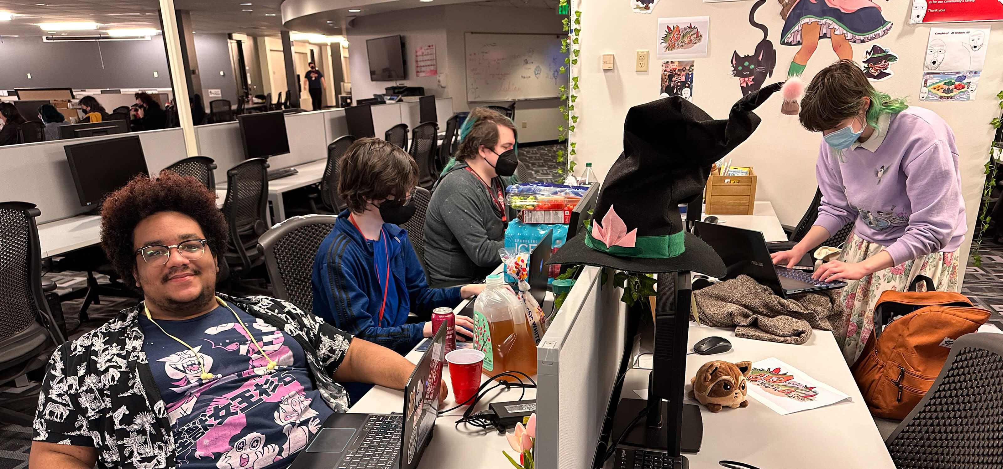 DigiPen students surrounded by snacks work on their Global Game Jam projects, one smiling for the camera.