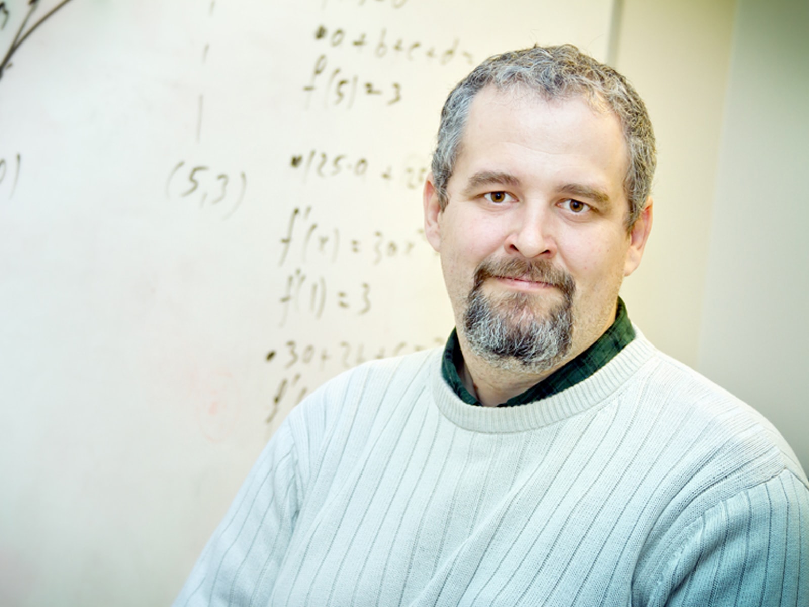 DigiPen mathematics professor Barnabas Bede smiling in front of a whiteboard decorated with mathematical formulas