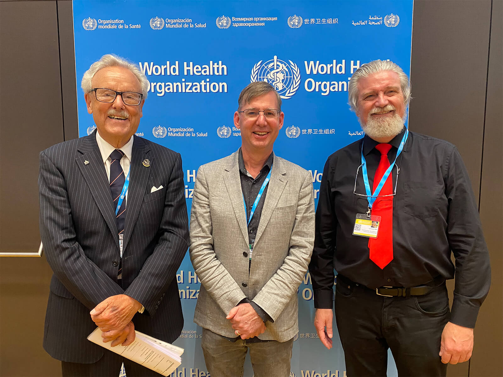 Brian Schmidt poses with two other summit attendees in front of a blue World Health Organization banner. 