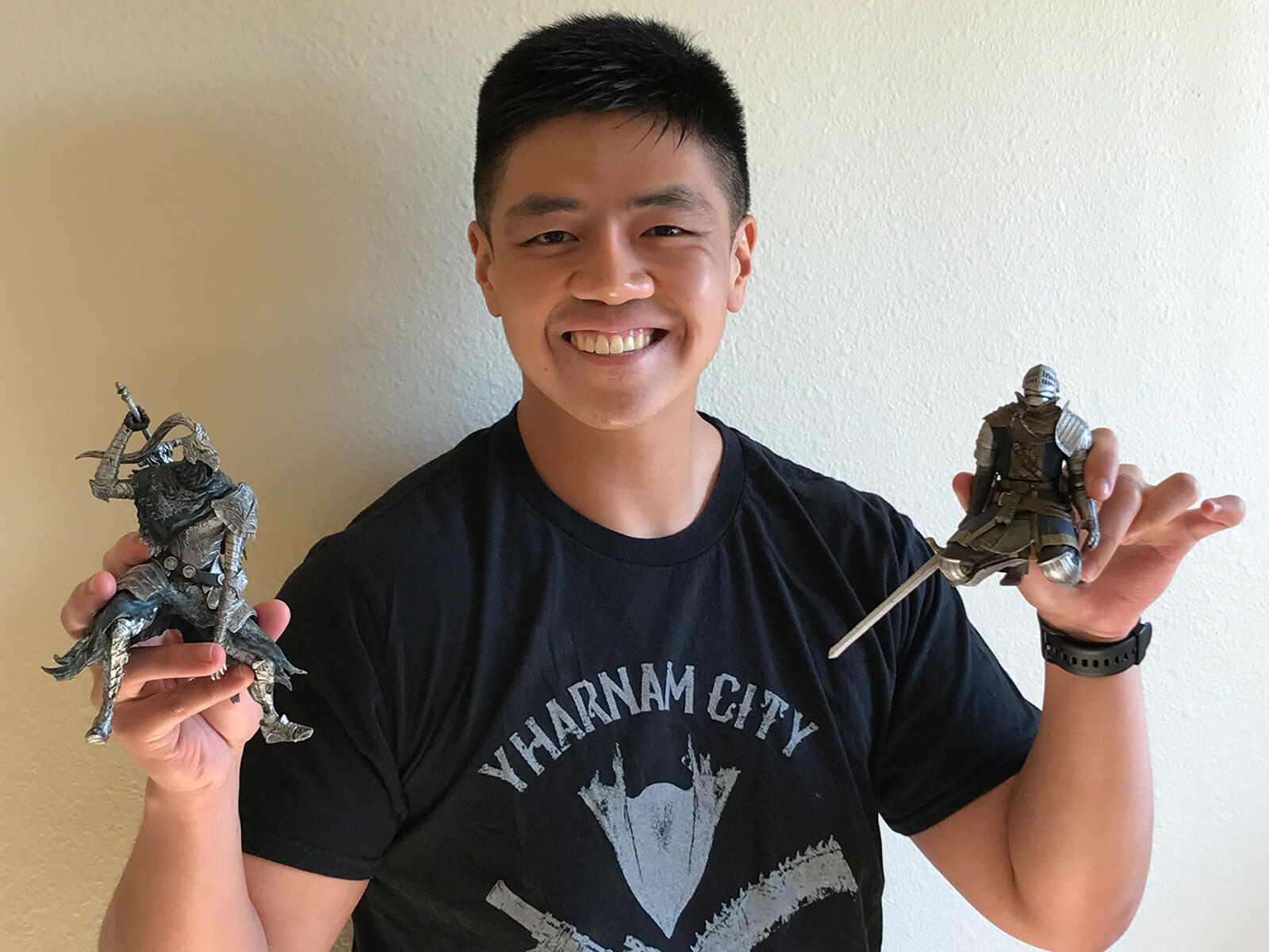 Cal Santiago smiles wearing a Bloodborne-themed shirt, holding two Dark Souls figurines.