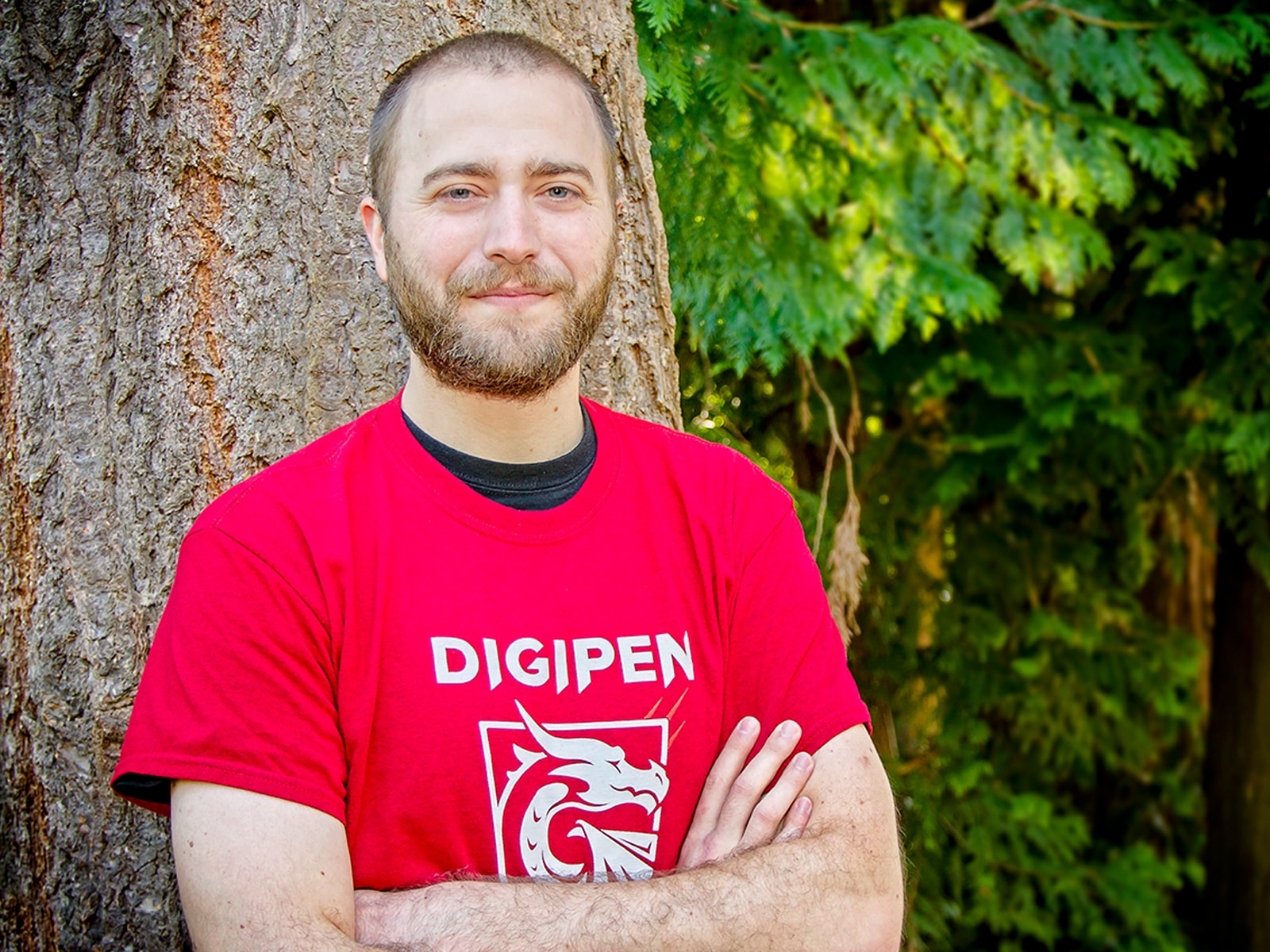 DigiPen student Casey Donelson leaning against a tree on the DigiPen campus with his arms crossed