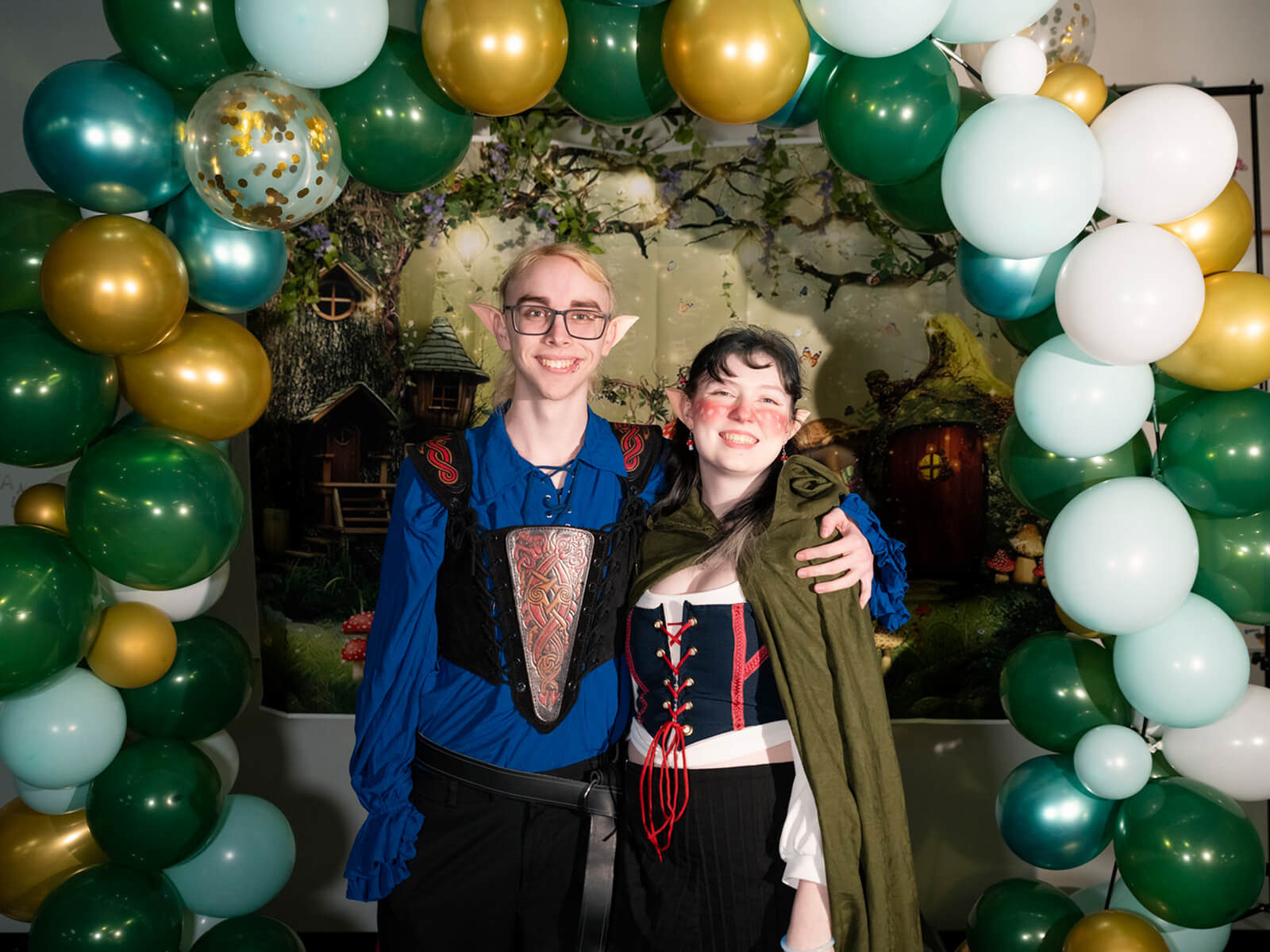Two DigiPen students dressed as elves pose in front of a balloon arch at the first annual DigiProm.