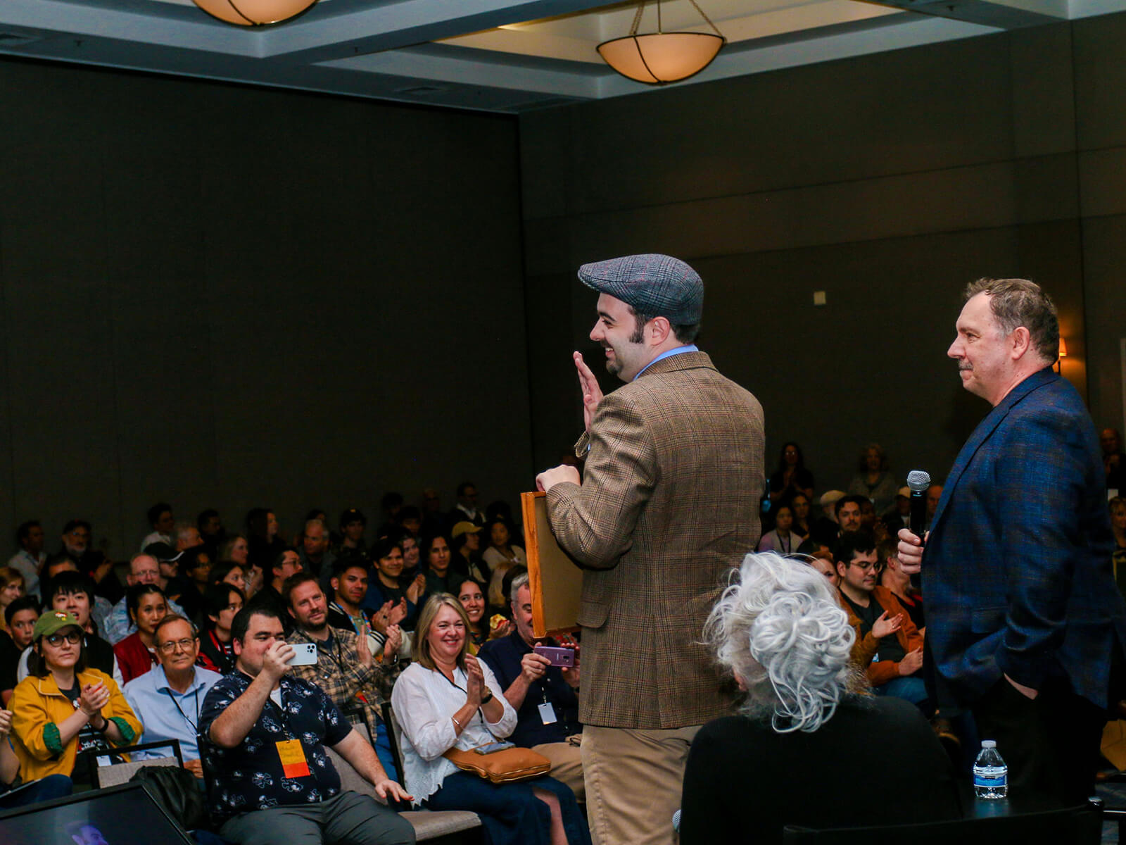 Edward Davies stands by Andreas Deja on stage at the CTN Expo and waves to an applauding crowd holding his award certificate.