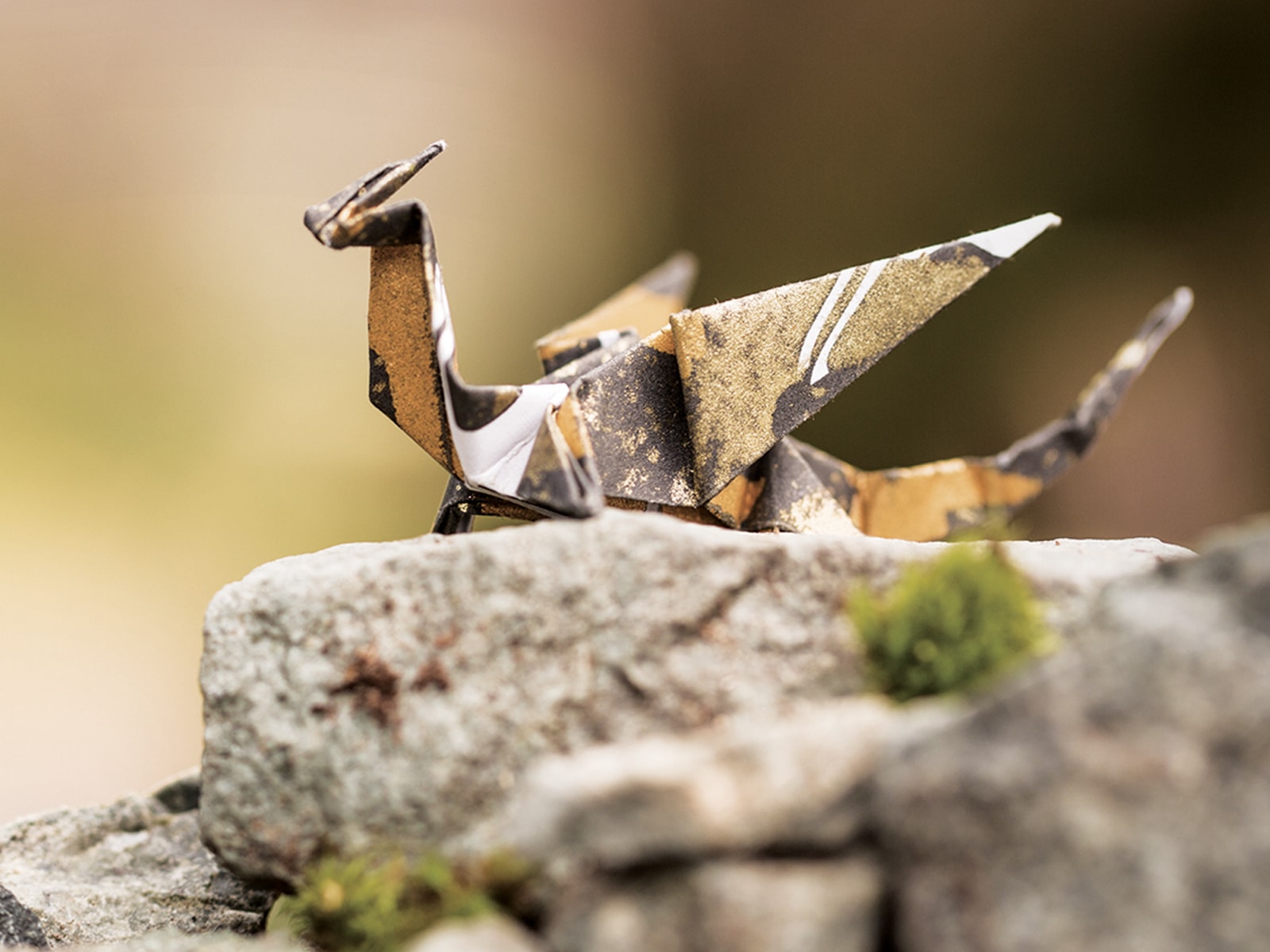 A gold and black origami dragon sitting on a mossy rock against a green background