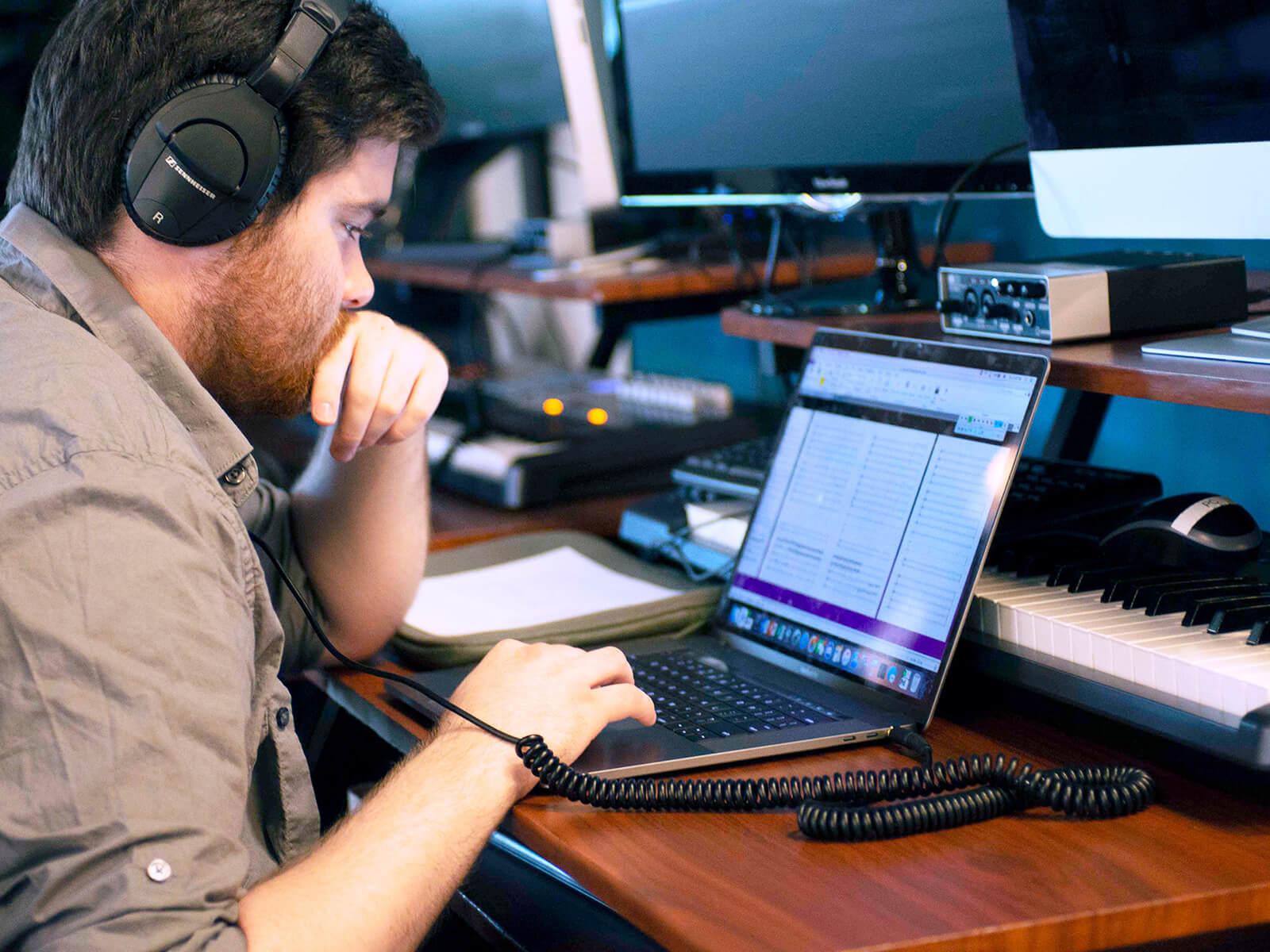 A DigiPen music student wearing headphones works at their laptop in front of a synthesizer.