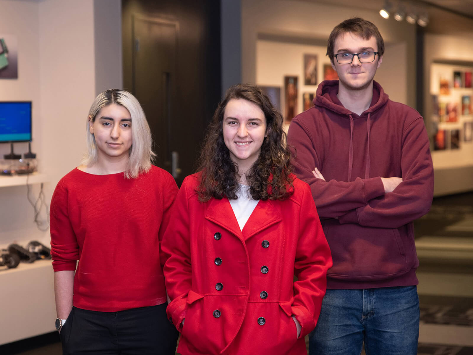 Three students stand next to computer engineering projects on display.