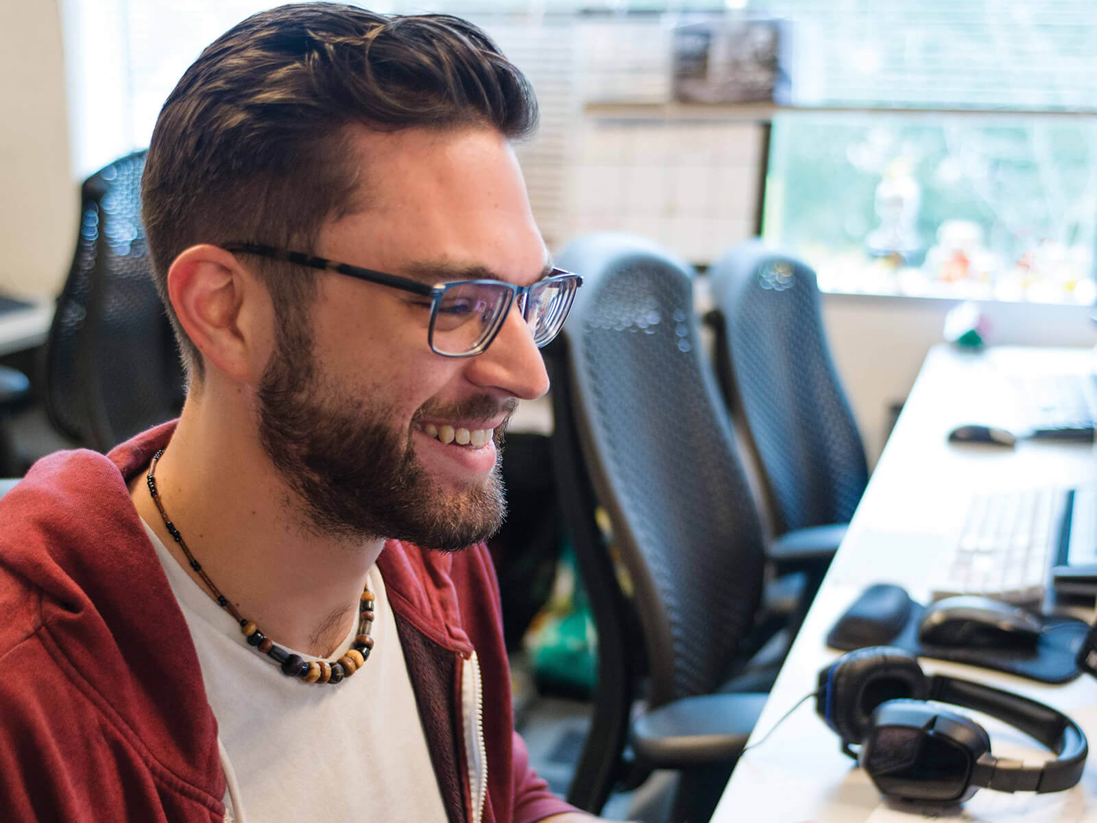 A student wearing glasses sits in a computer lab smiling at his computer screen.