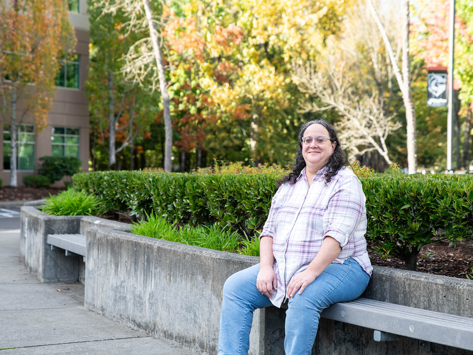 Ellen Beeman sits on a bench outside campus on a sunny day