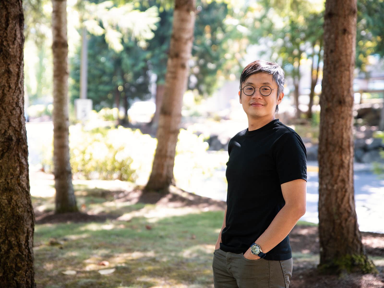 DigiPen instructor YZ Tan smiles with his hands in his pockets on a grassy, tree-filled lot.