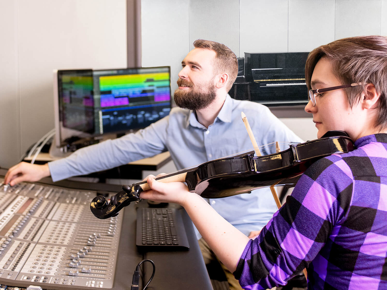 A DigiPen student plays violin next to a large audio mixing board.