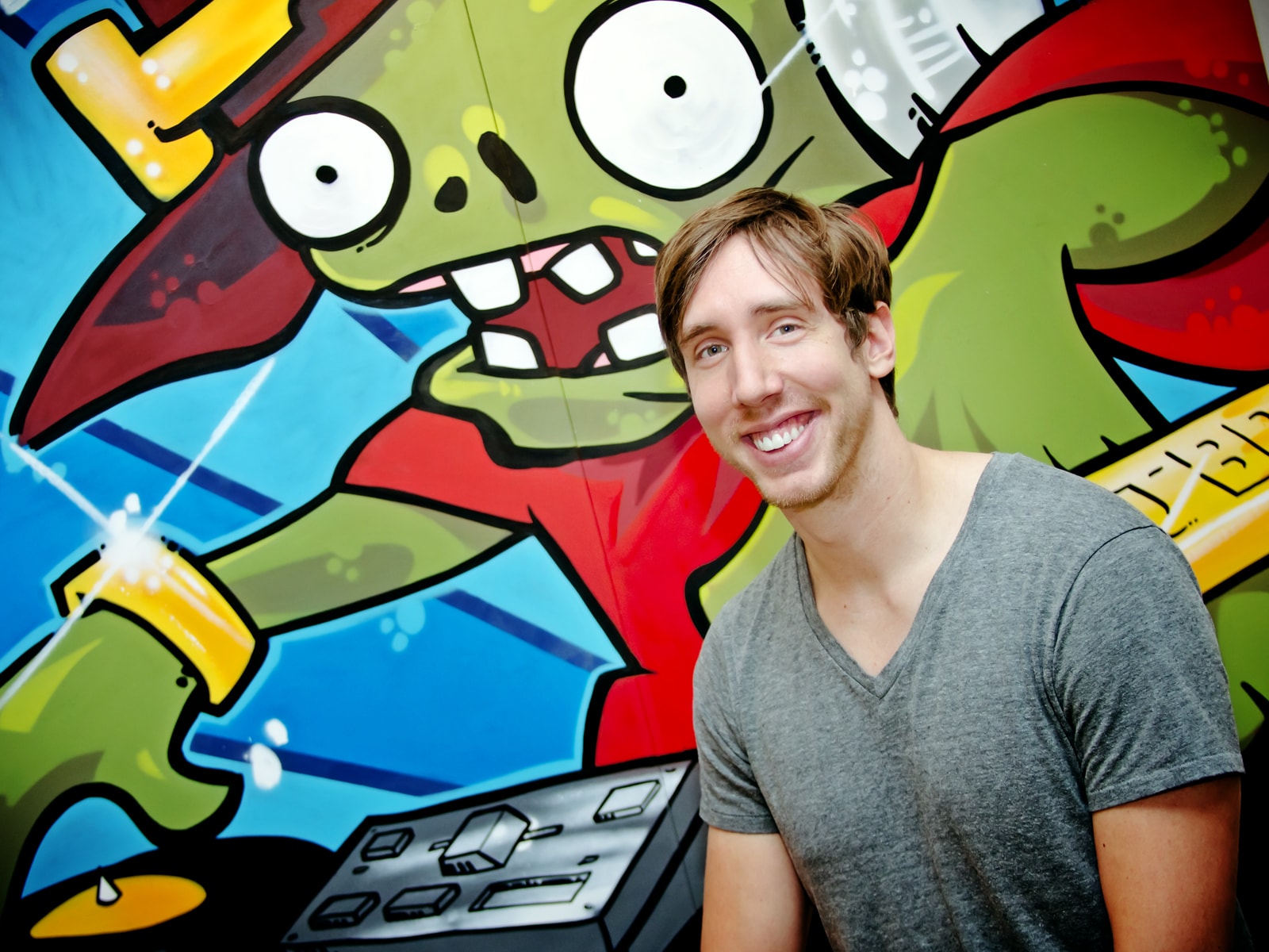DigiPen BFA alumnus Mark Barrett smiling in front of large grafffiti-style wall painting of a zombie at PopCap's office