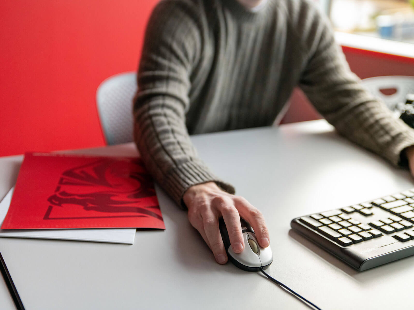 Angled view of a male faculty member using a mouse next to a DigiPen branded red folder