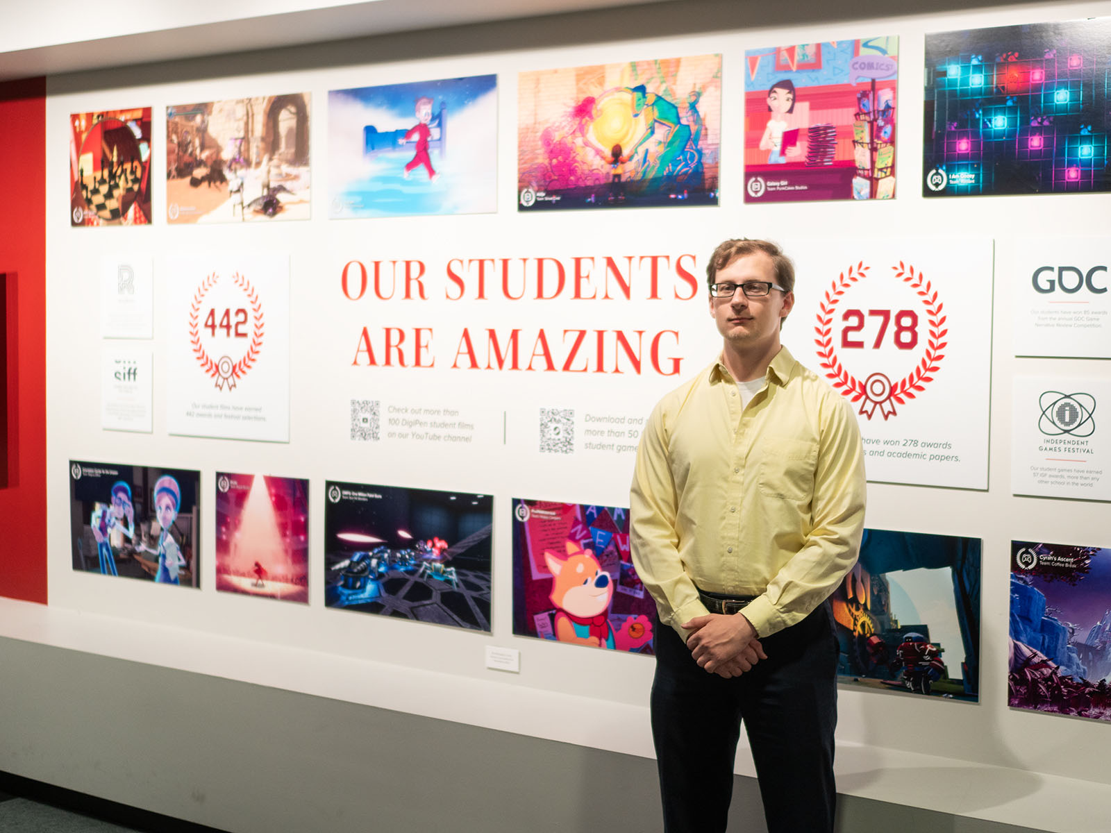 Joseph Crump poses with his hands folded in front of a DigiPen campus hallway display.