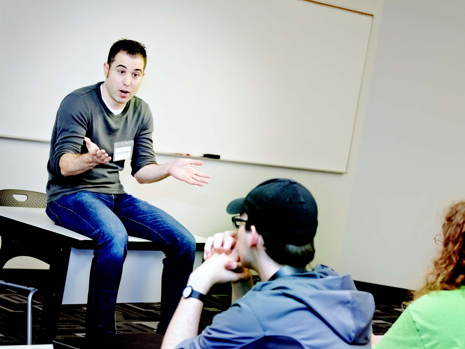 Mike Ambinder sitting on a table, talking to students in a DigiPen classroom