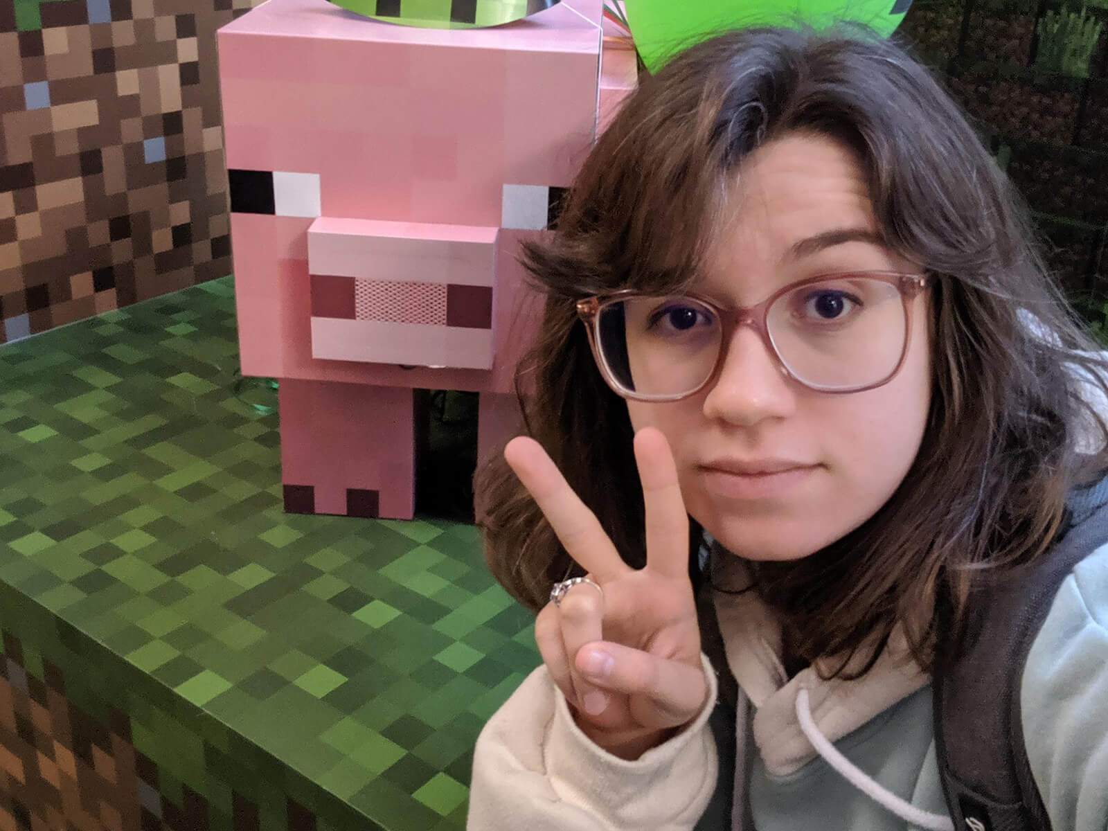 DigiPen graduate and Mojang artist Kelly Greene flashes a peace sign next to Minecraft Earth’s Muddy Pig