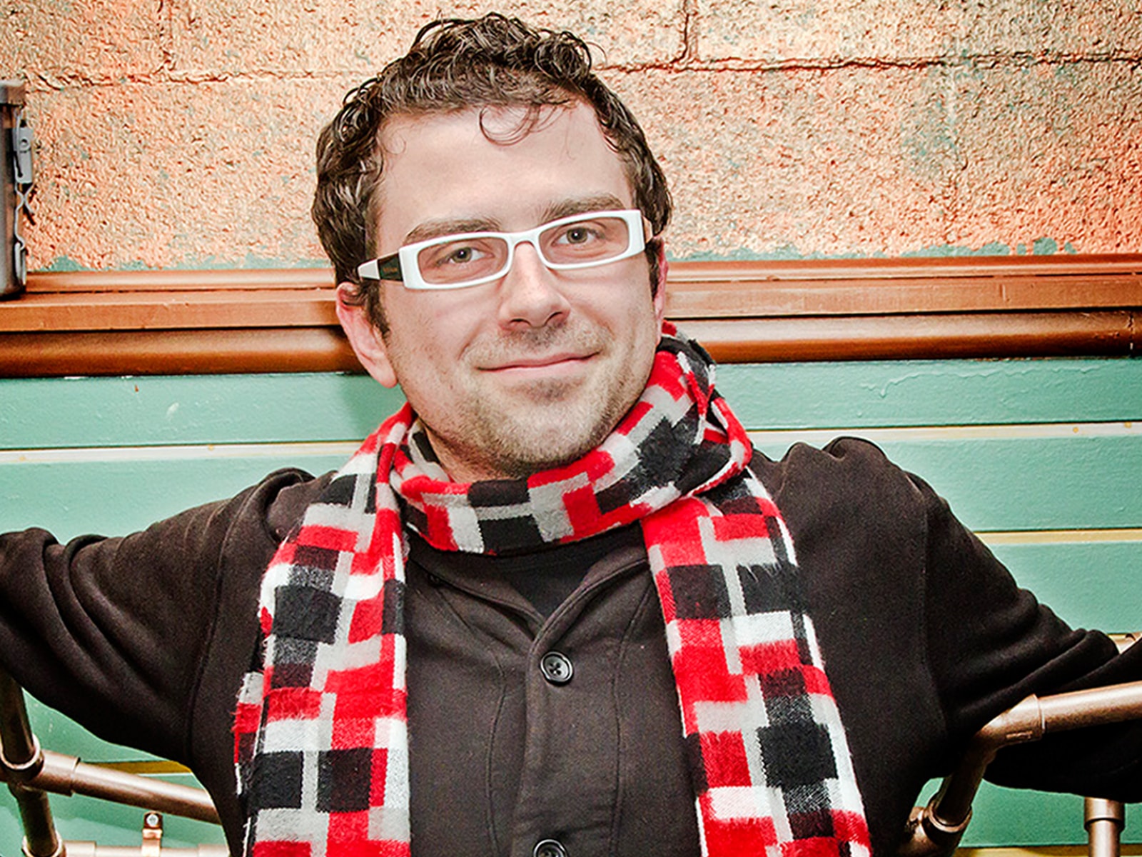 DigiPen alumnus Nate Martin in a plaid scarf, black coat and white-framed glasses with a prop made of bronze-colored pipes