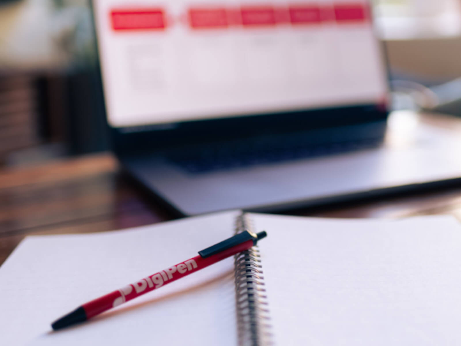 A pen and open notebook in front of a laptop.