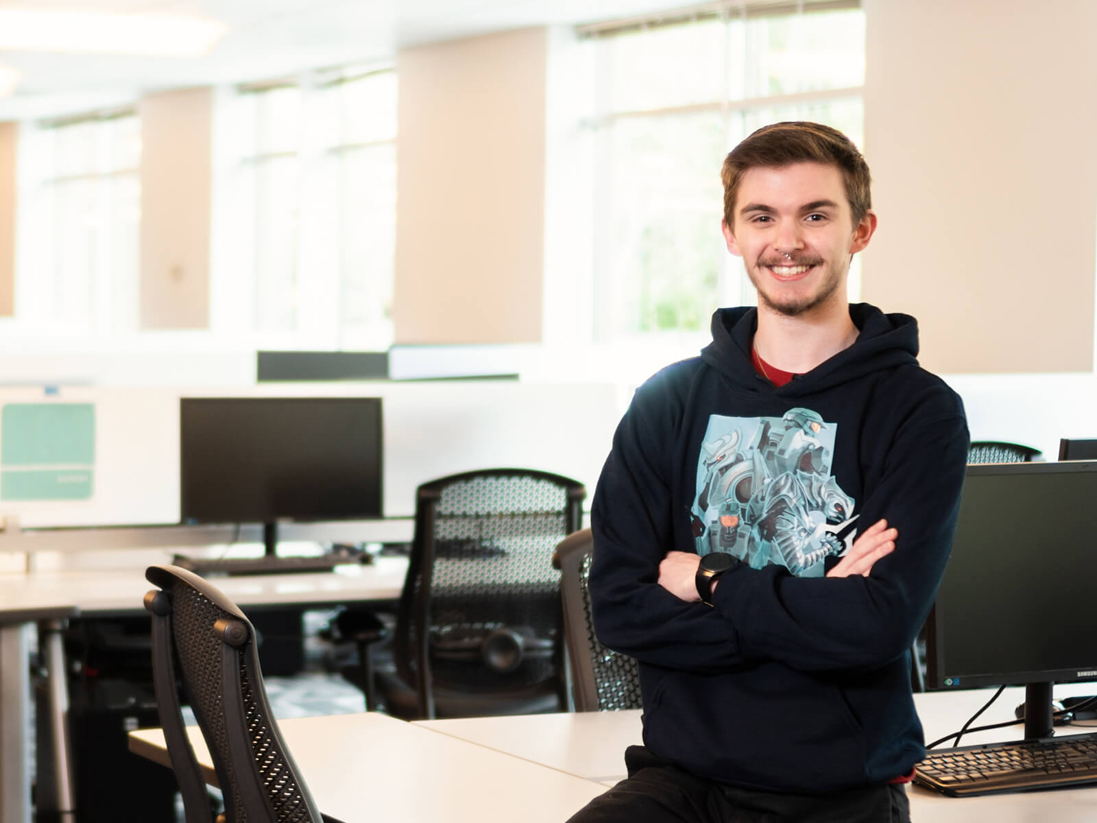 DigiPen Student of the Year Brandon Stam poses with their arms crossed in the campus lab.