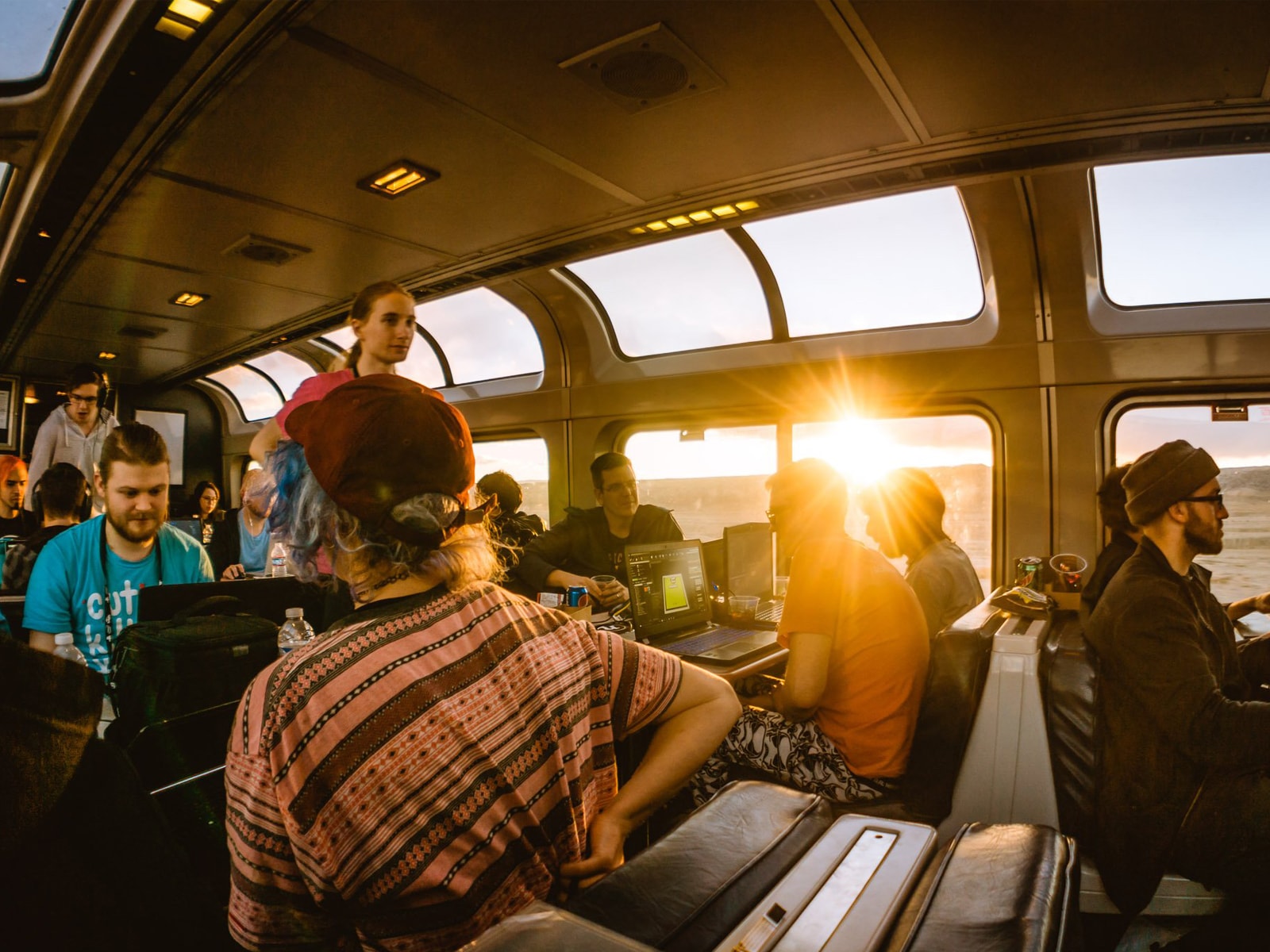 Afternoon sun beaming through the windows of the train's observation car where gamers collaborate on their laptops