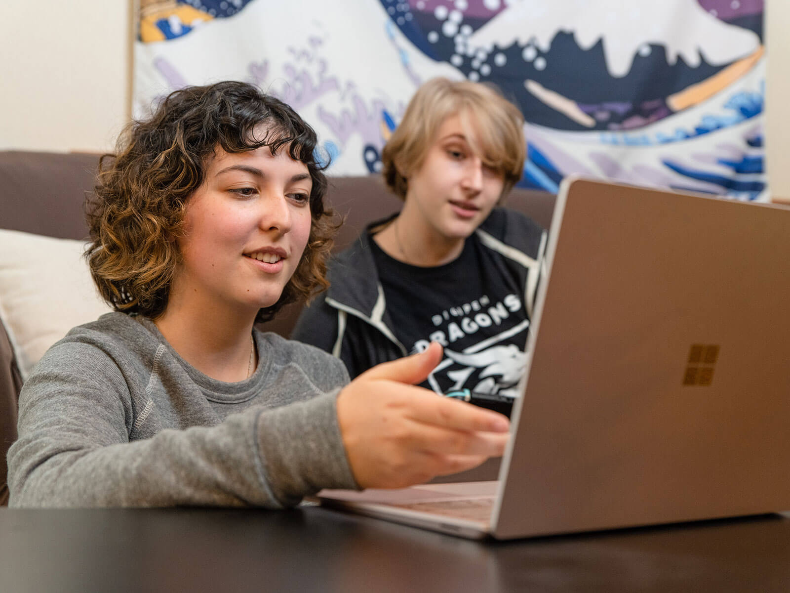 A female and male student sit and look at laptop while conversing 