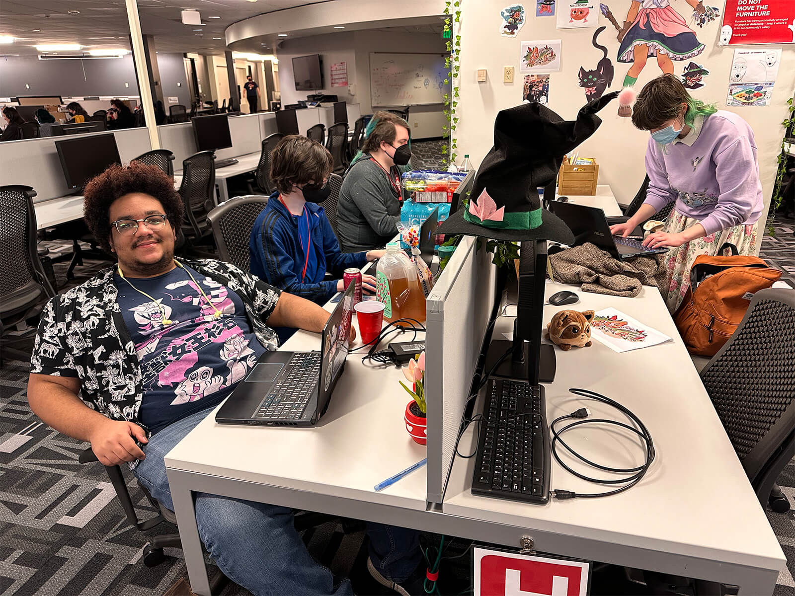 DigiPen students surrounded by snacks work on their Global Game Jam projects, one smiling for the camera.