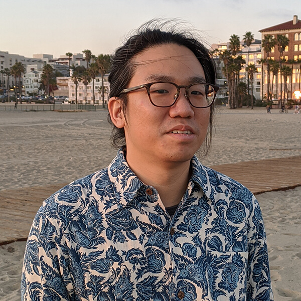 DigiPen graduate Chia-Hao Ching poses on a beach lined with palm trees.