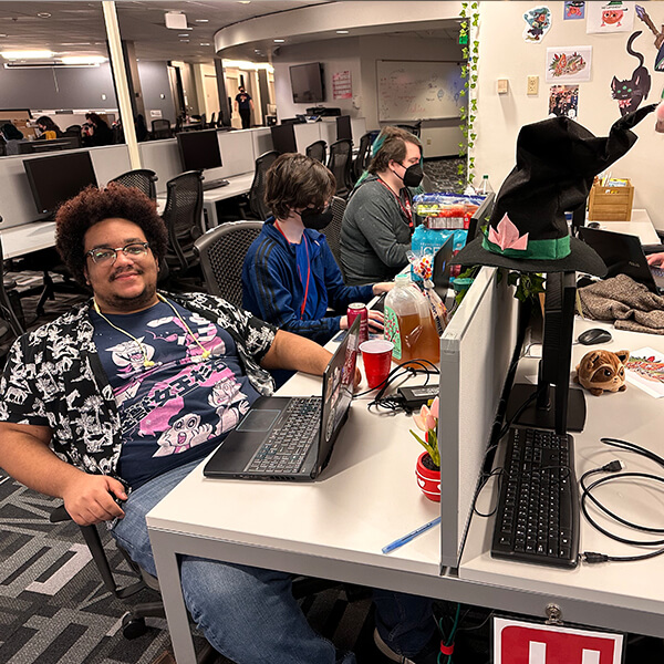 DigiPen students surrounded by snacks work on their Global Game Jam projects, one smiling for the camera.