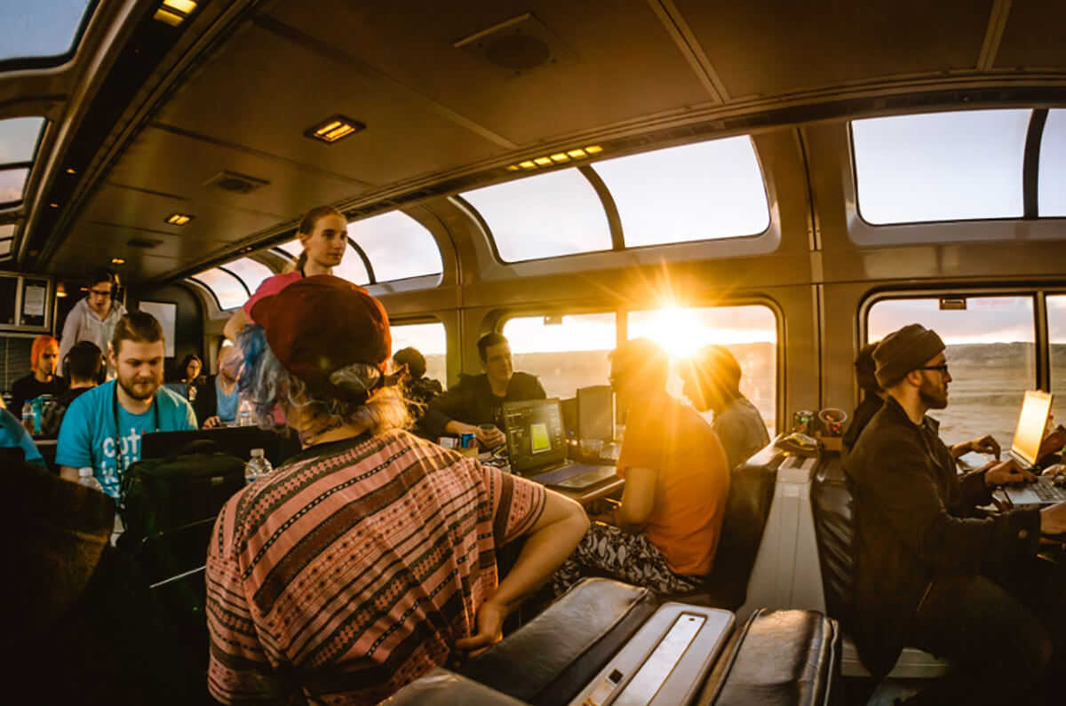 Afternoon sun beaming through the windows of the train's observation car where gamers collaborate on their laptops