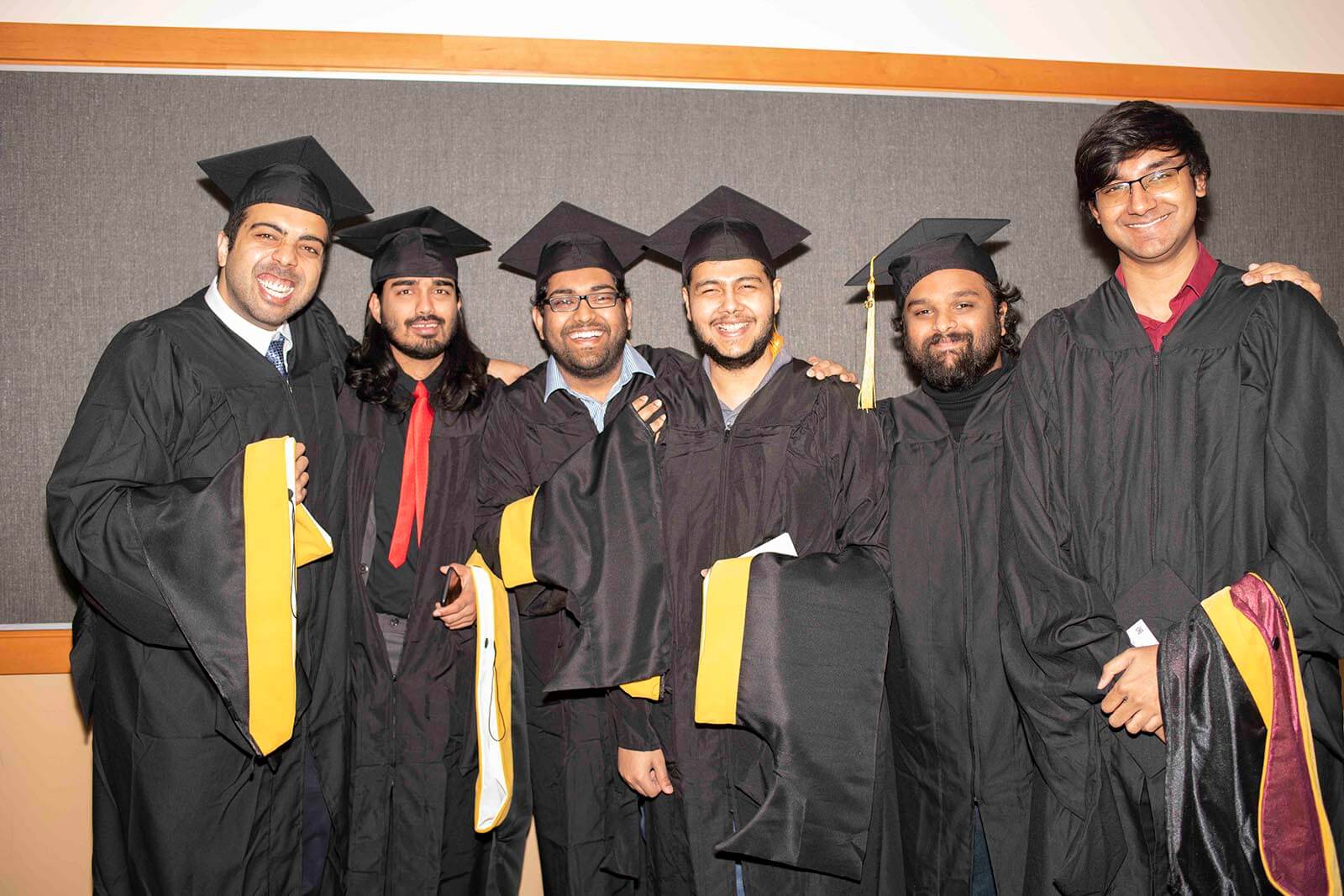 A group of master's degree students pose in graduate robes and mortarboards holding their colored candidate hoods.