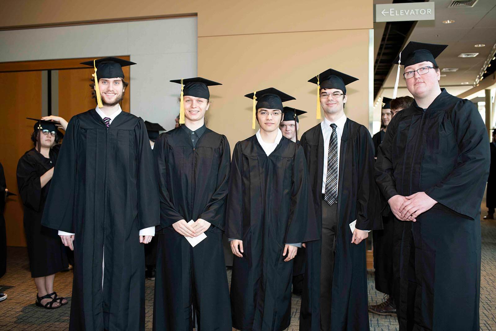 A group of graduating students pose in black robes and mortarboards in a hallway.