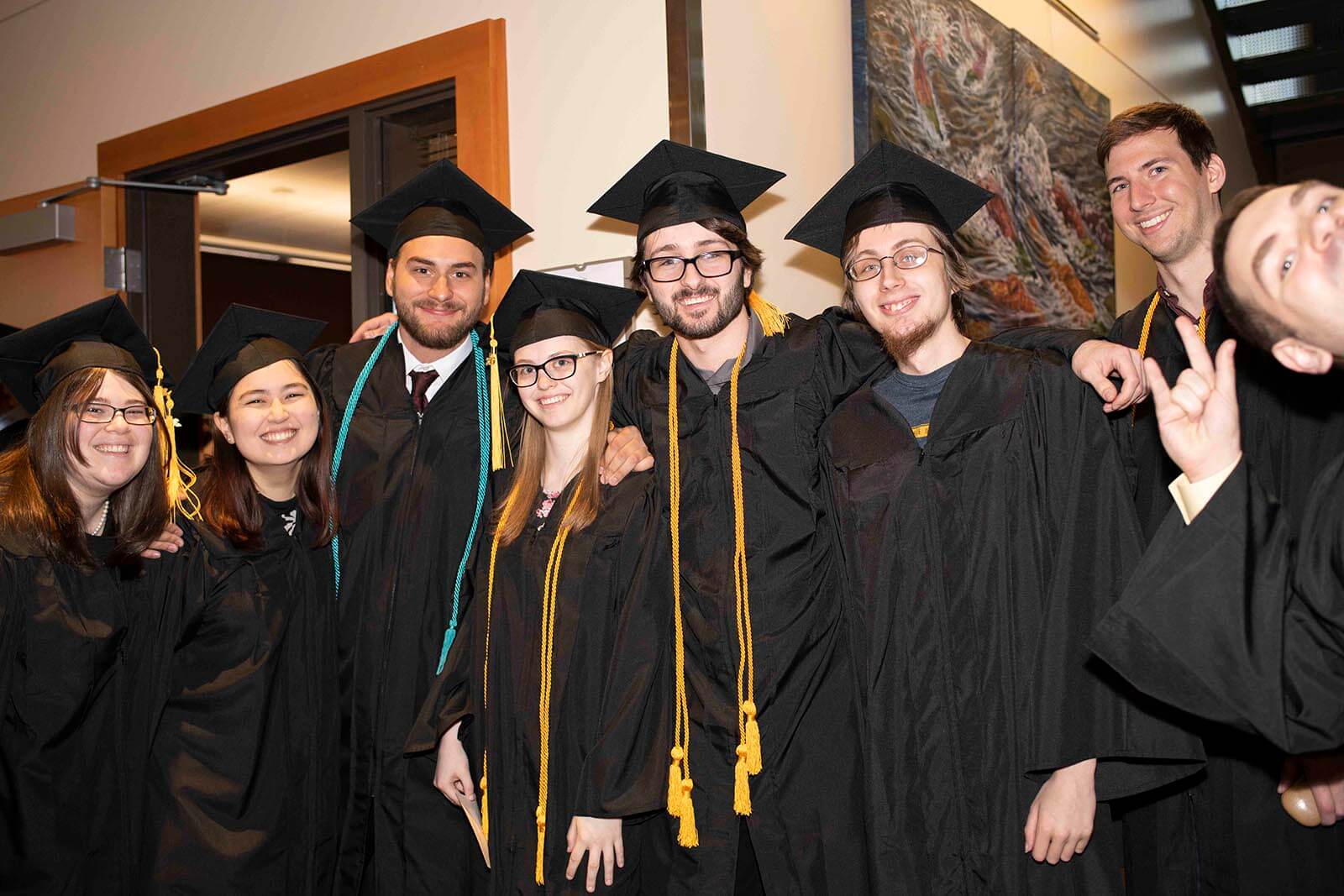 A group of graduating students in robes and mortarboards pose for a photo in a convention center hallway.