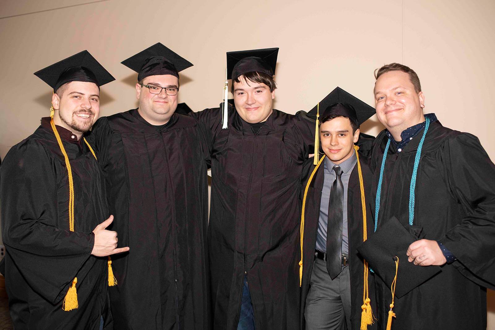 A group of graduating students in robes and mortarboards pose for a photo in a hallway.