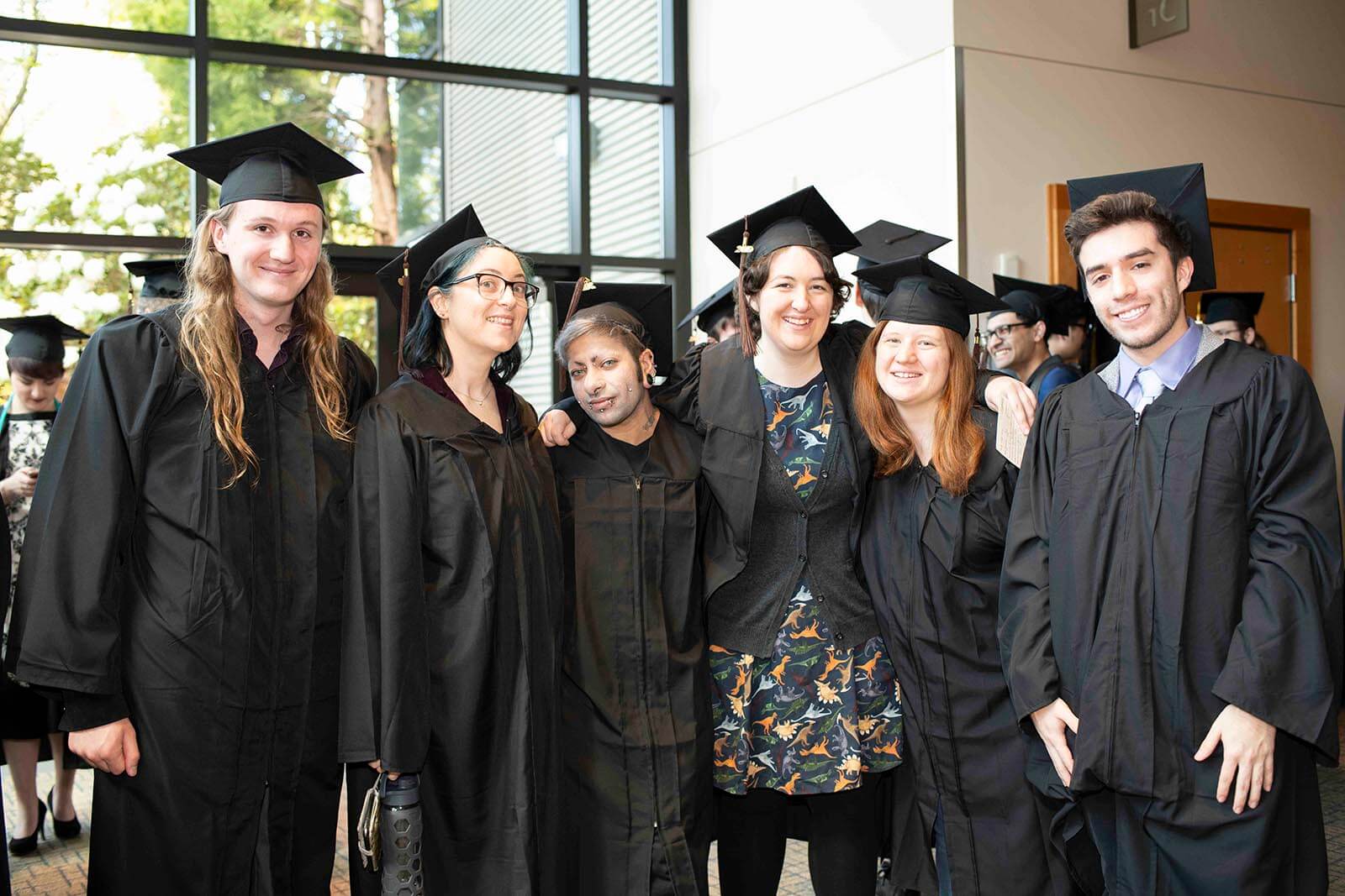 A group of graduating students in robes and mortarboards pose for a photo in a lobby area.