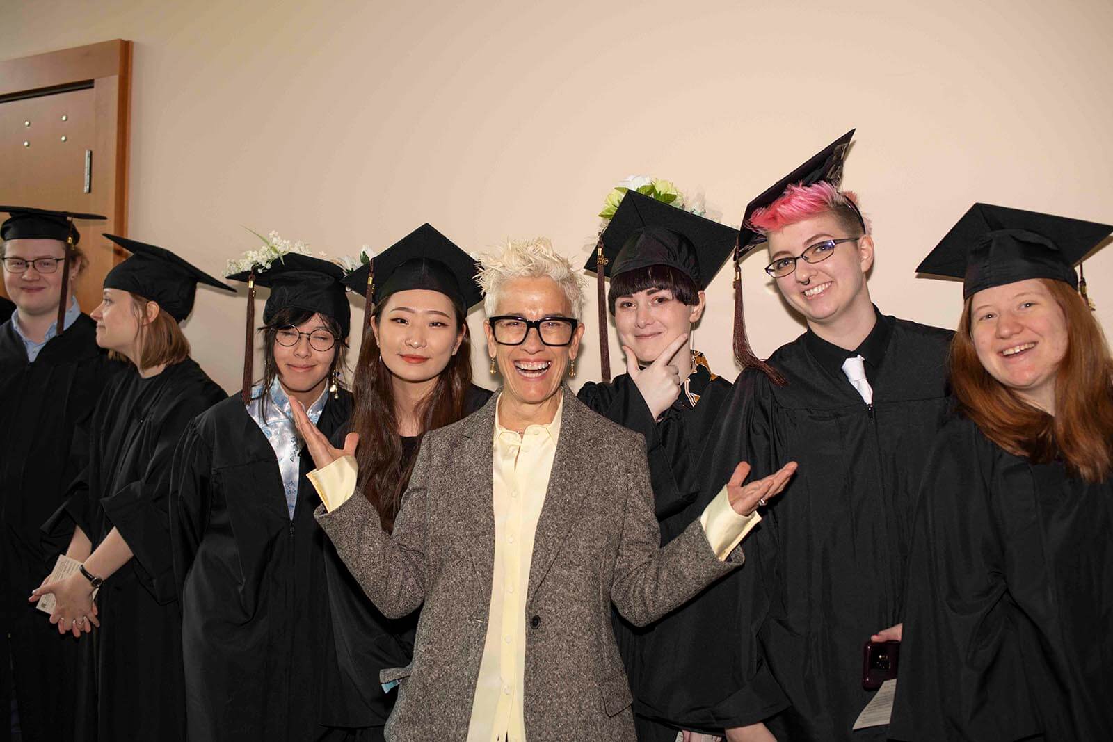 Patti Dobrowolski smiles posing with a group of students in graduate robes and mortarboards.