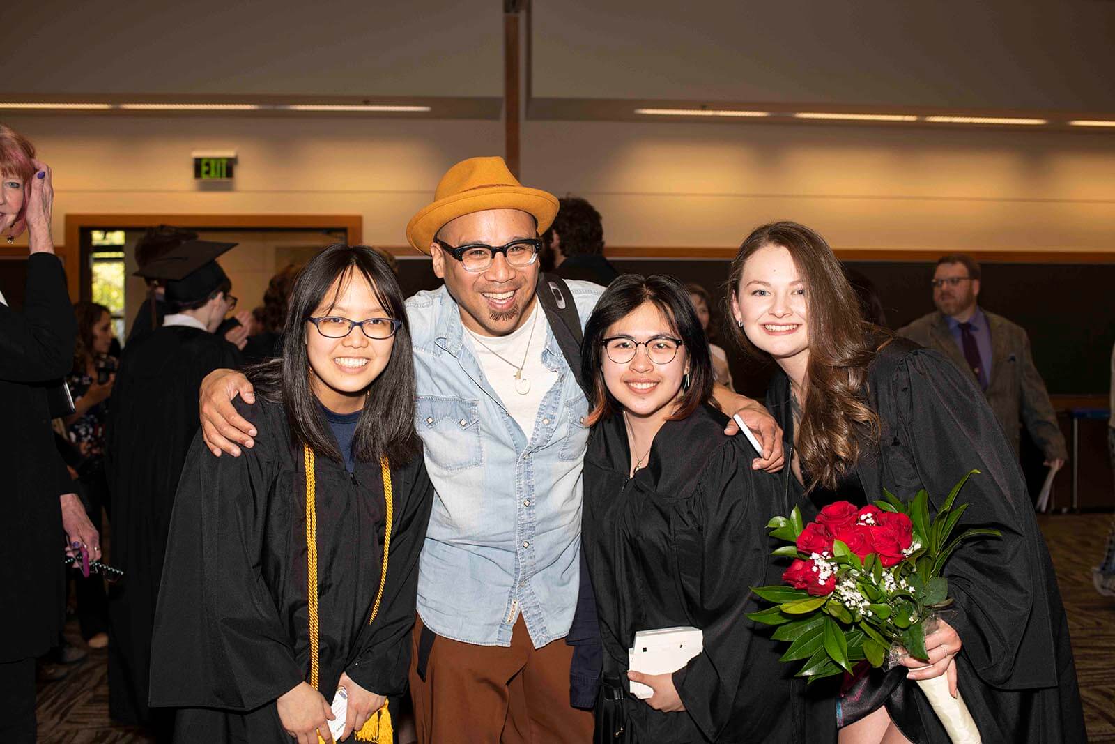 Newly graduated students in black robes pose with a DigiPen instructor in a convention center meeting room.