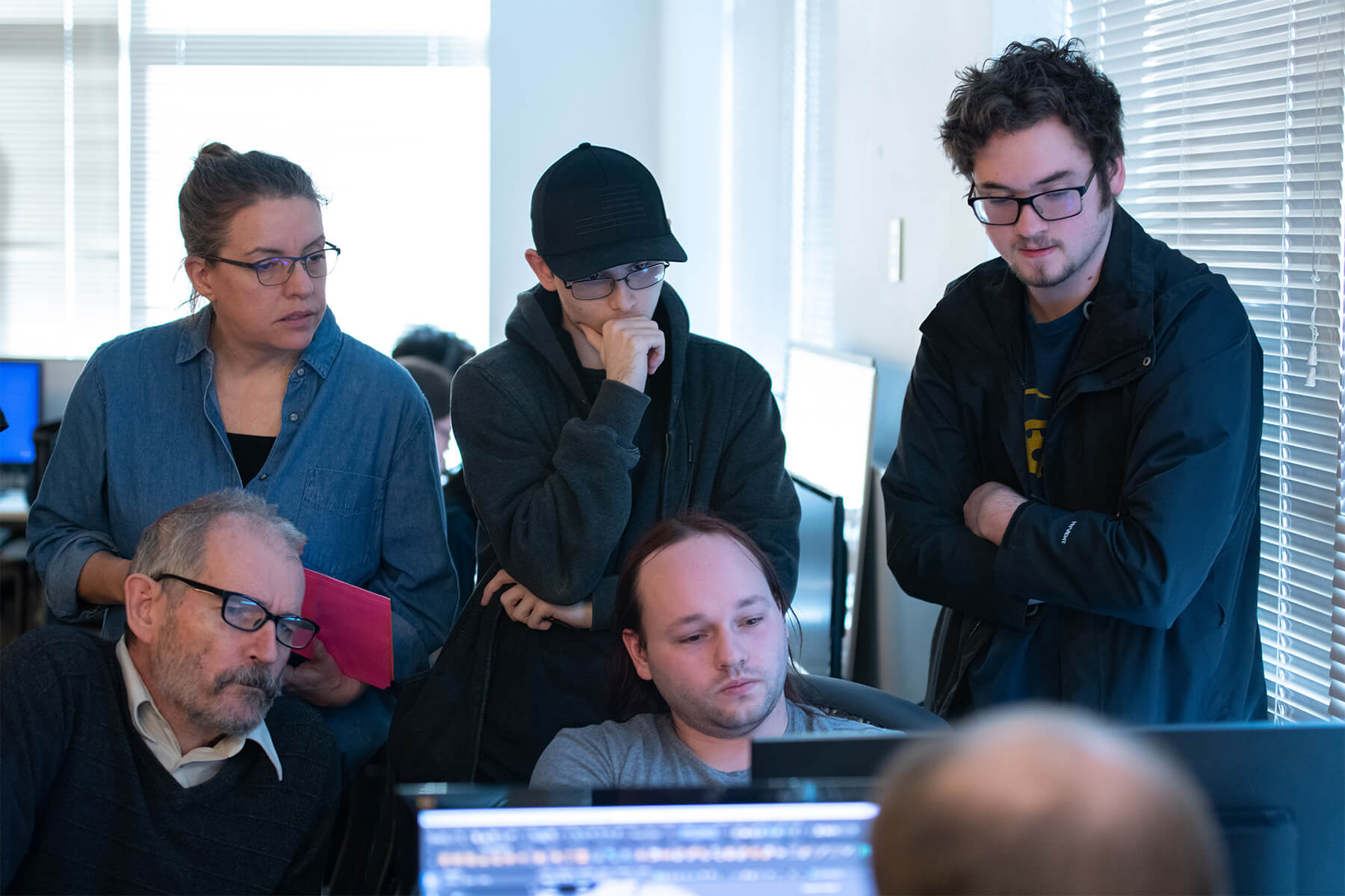 Two DigiPen professors look at three students’ game team project on a computer screen in a campus production lab.