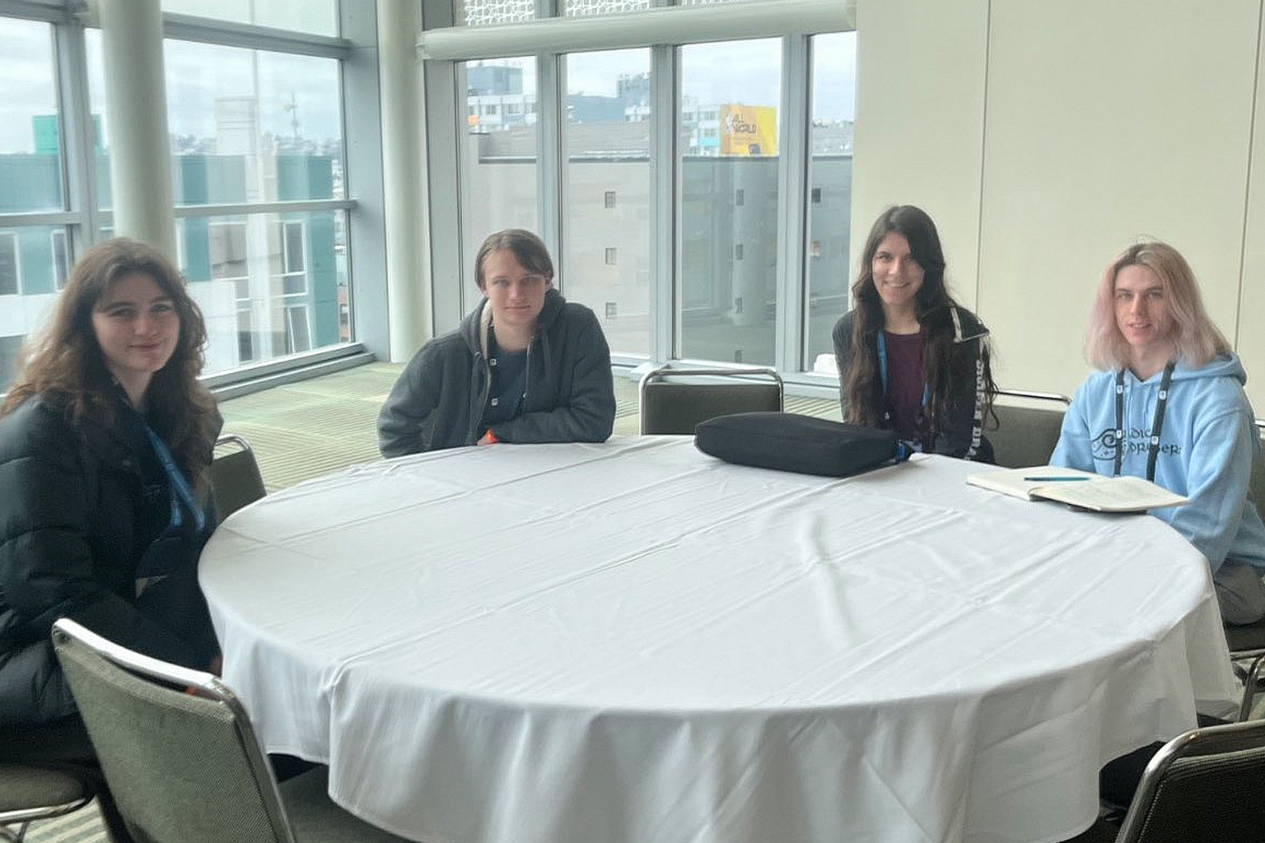 Four DigiPen students sit around a white table in a window-lined room, smiling for the camera.