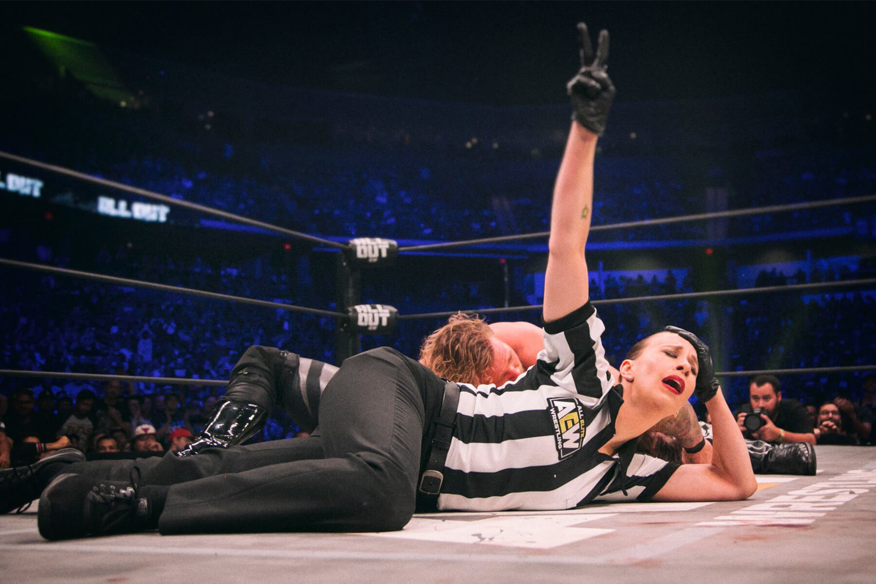 Aubrey Edwards lays on the mat of the wrestling ring and flashes a peace sign at AEW’s All Out.