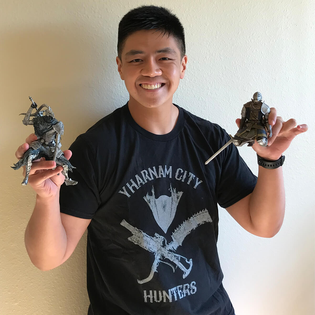 Cal Santiago smiles wearing a Bloodborne-themed shirt, holding two Dark Souls figurines.