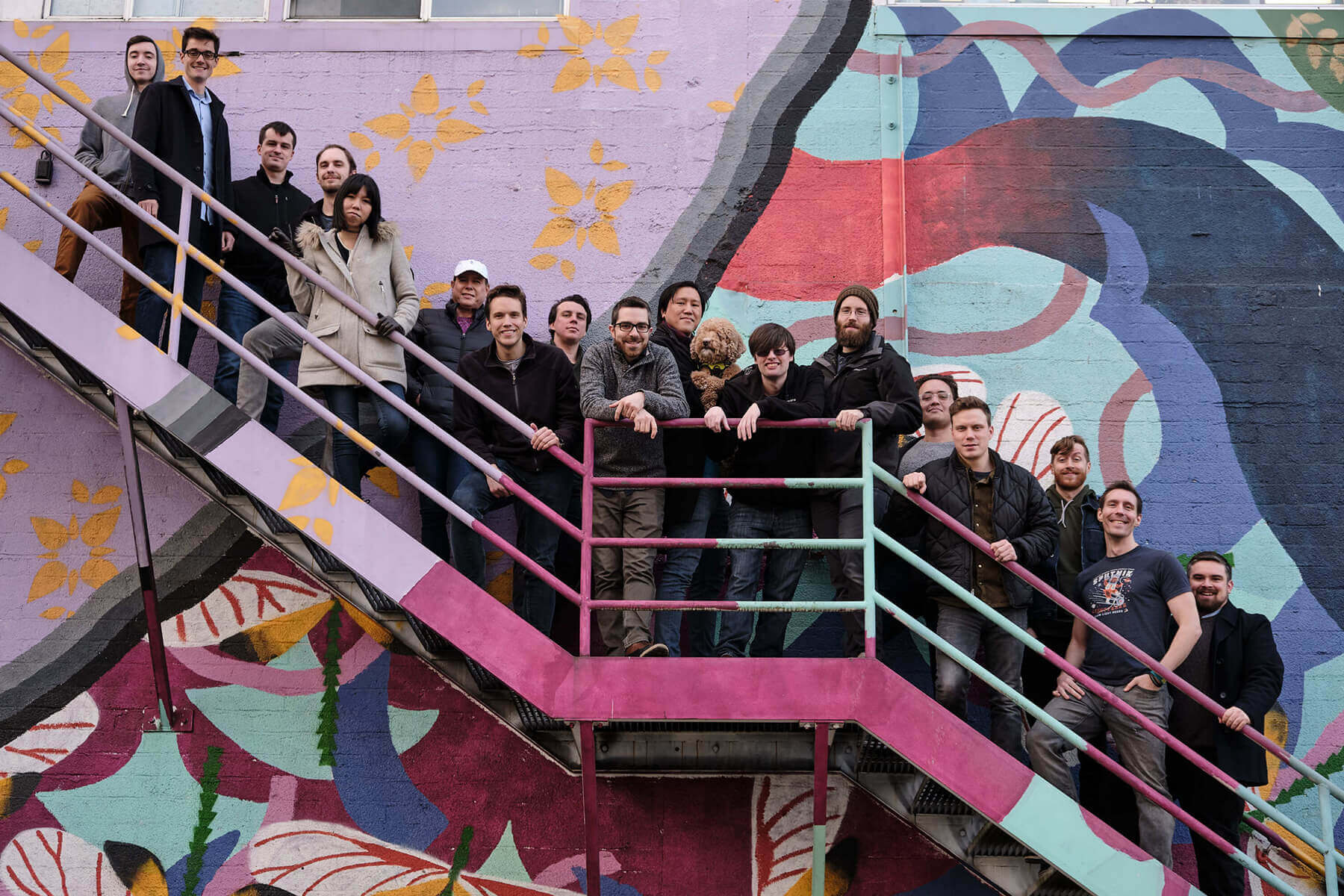 The staff of alumni-founded game studio Giant Enemy Crab pose on a staircase