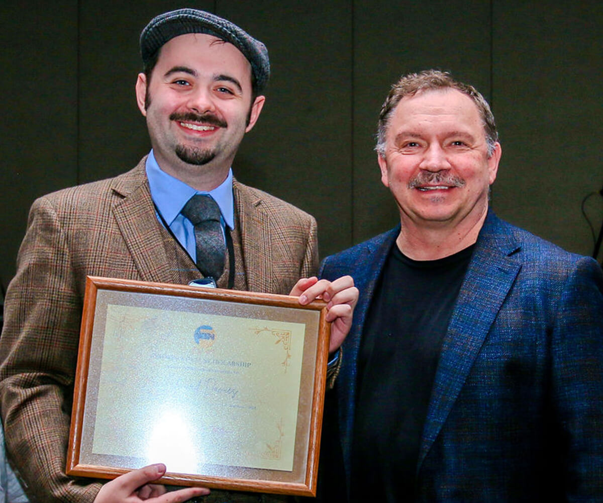 Edward Davies holds his framed award certificate next to a smiling Andreas Deja.