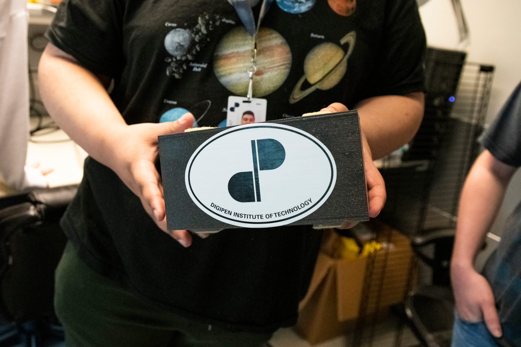 Student holds 3D-printed box bearing a DigiPen sticker.